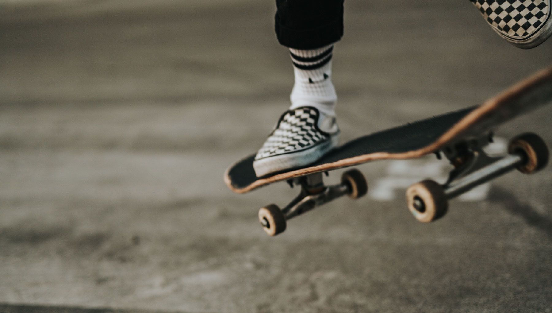 A person's feet in checkered shoes on a skateboard. - Skate