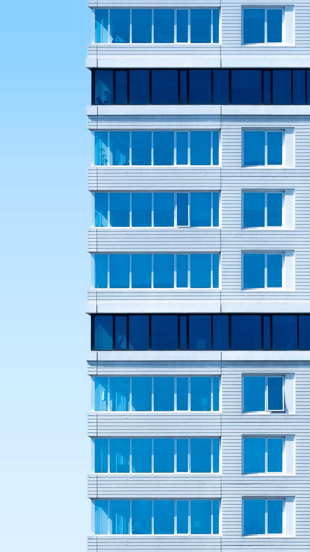 A tall white building with blue windows - Architecture