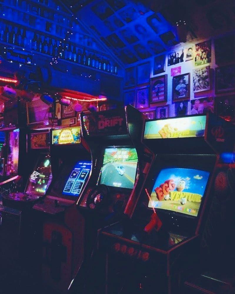 A room full of old school arcade games with neon lights. - Arcade