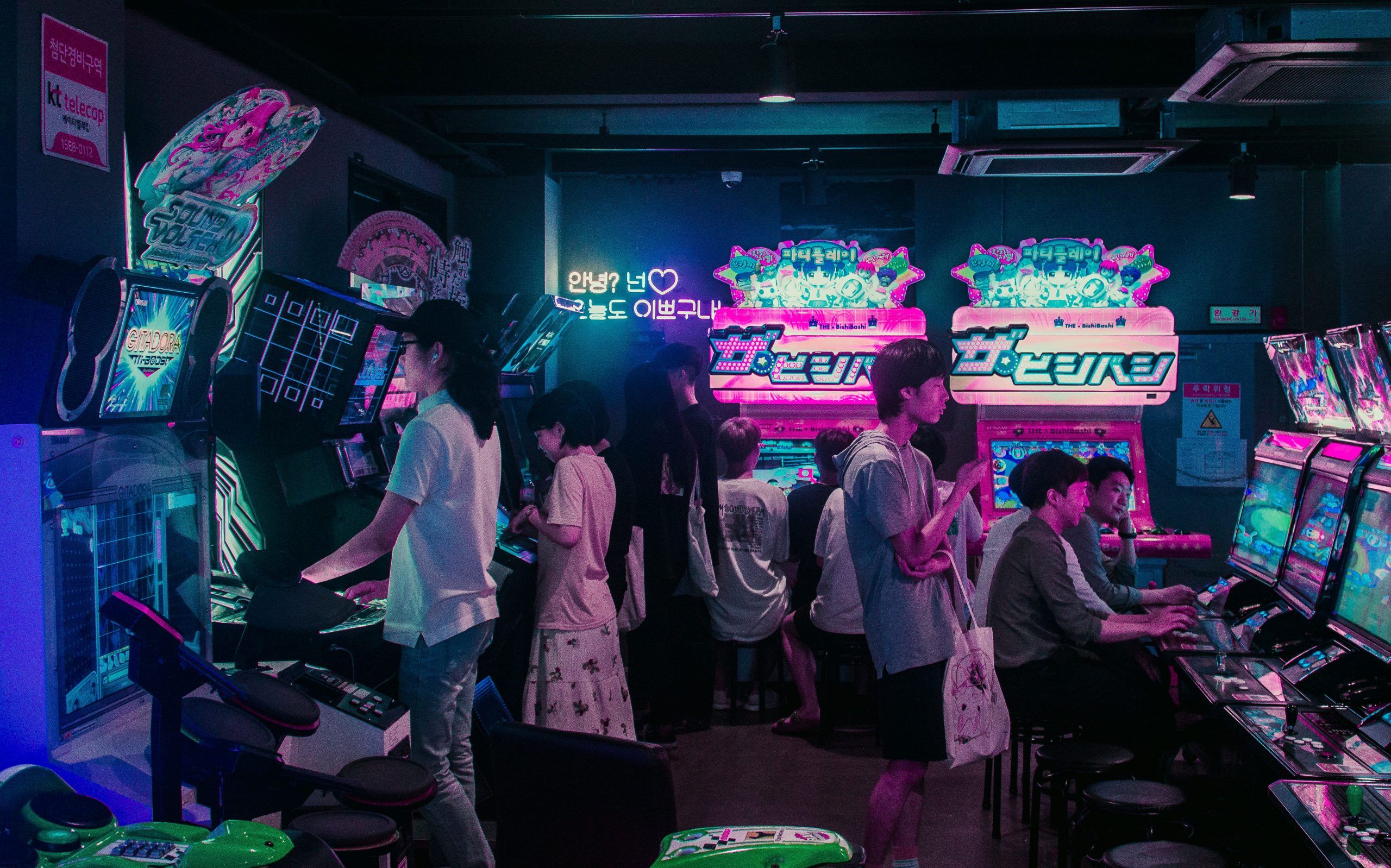 A group of people playing video games in a dark room with neon lights. - Arcade
