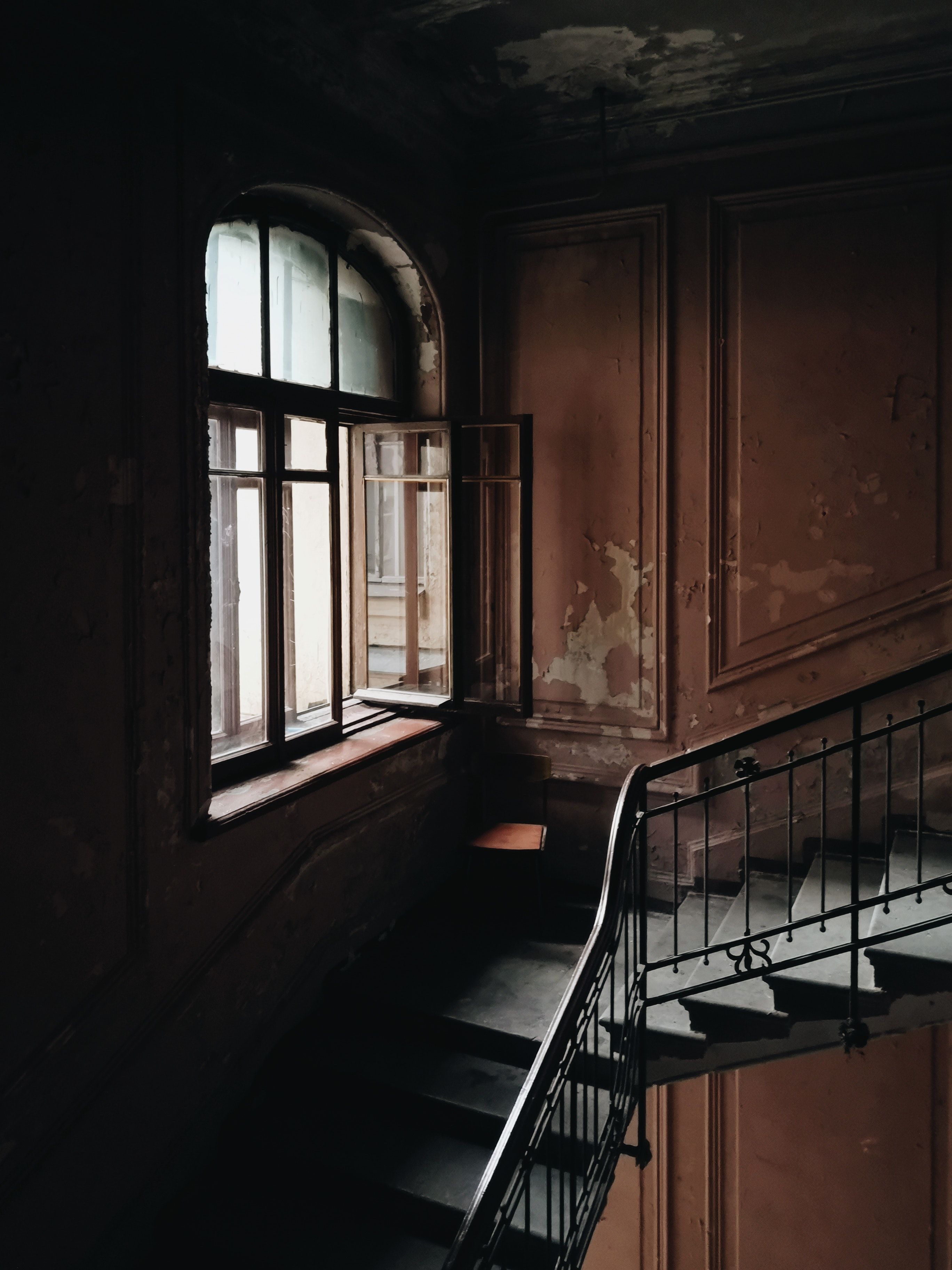 A dark stairwell with a rusted railing and a window letting in light. - Black, sad
