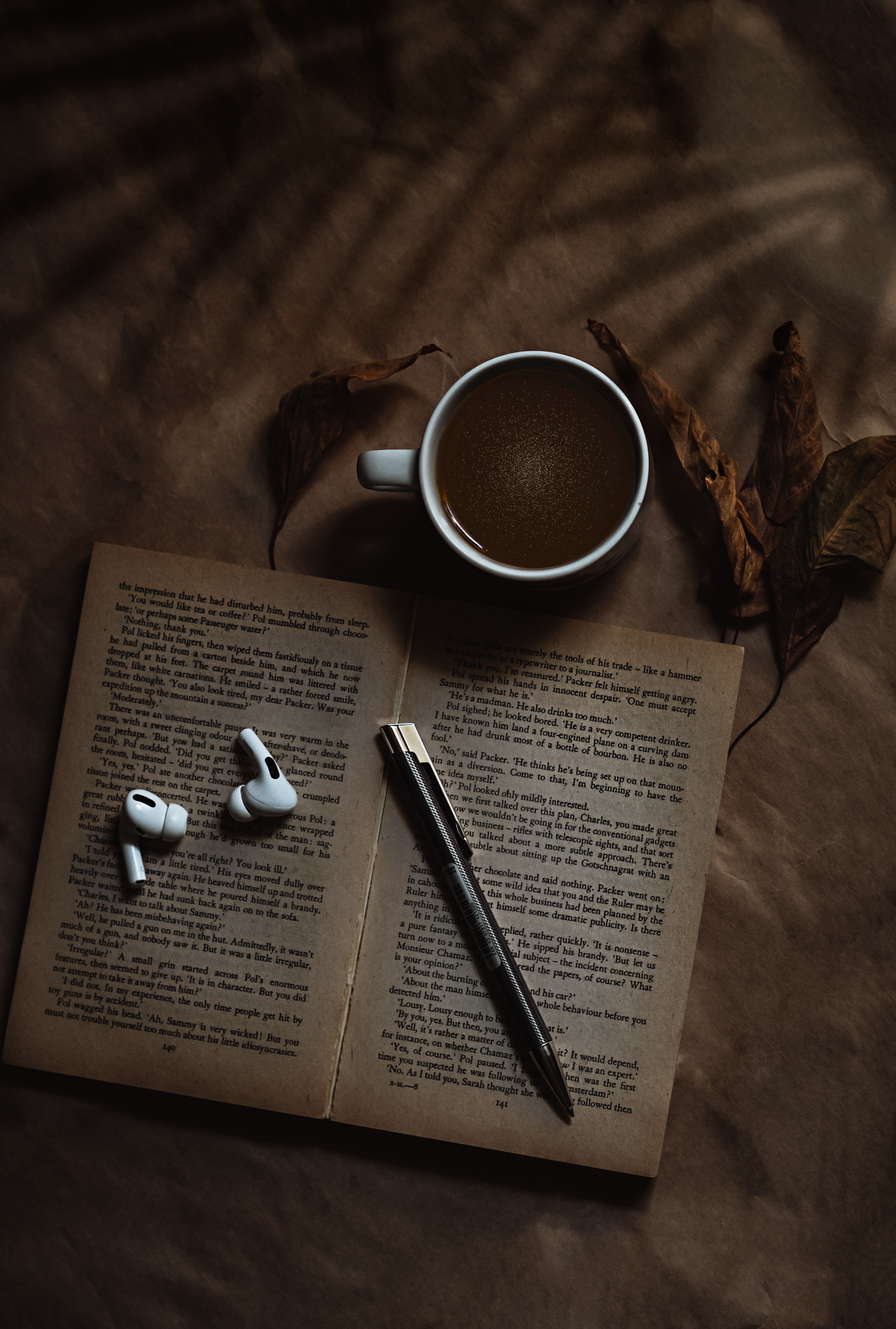 A book, a cup of coffee, a pen and earphones on a bed. - Coffee