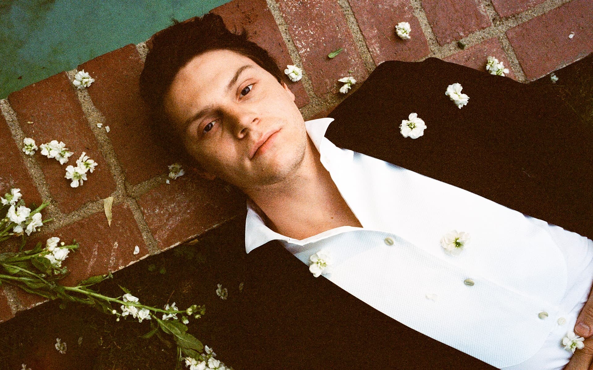 A man laying down with flowers on his face - Evan Peters