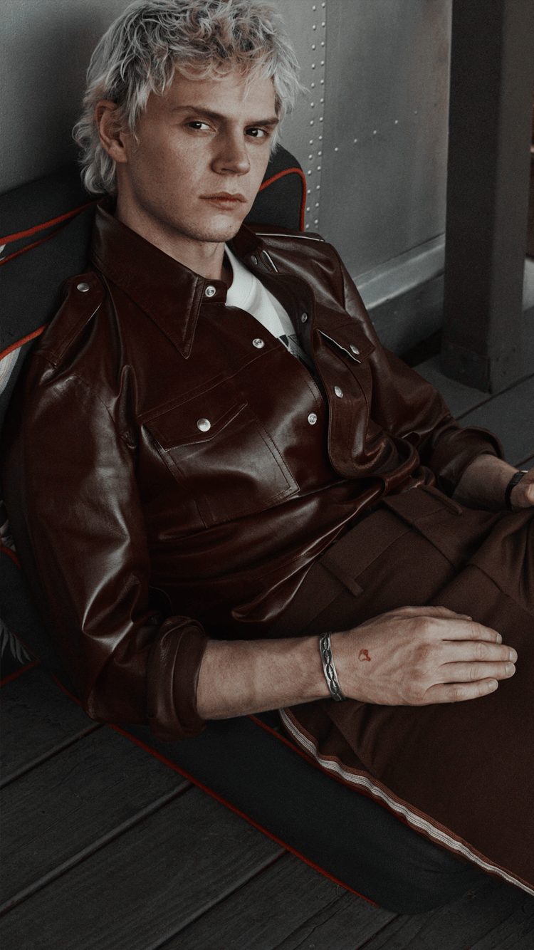 A man with bleached hair wearing a brown leather jacket and trousers - Evan Peters