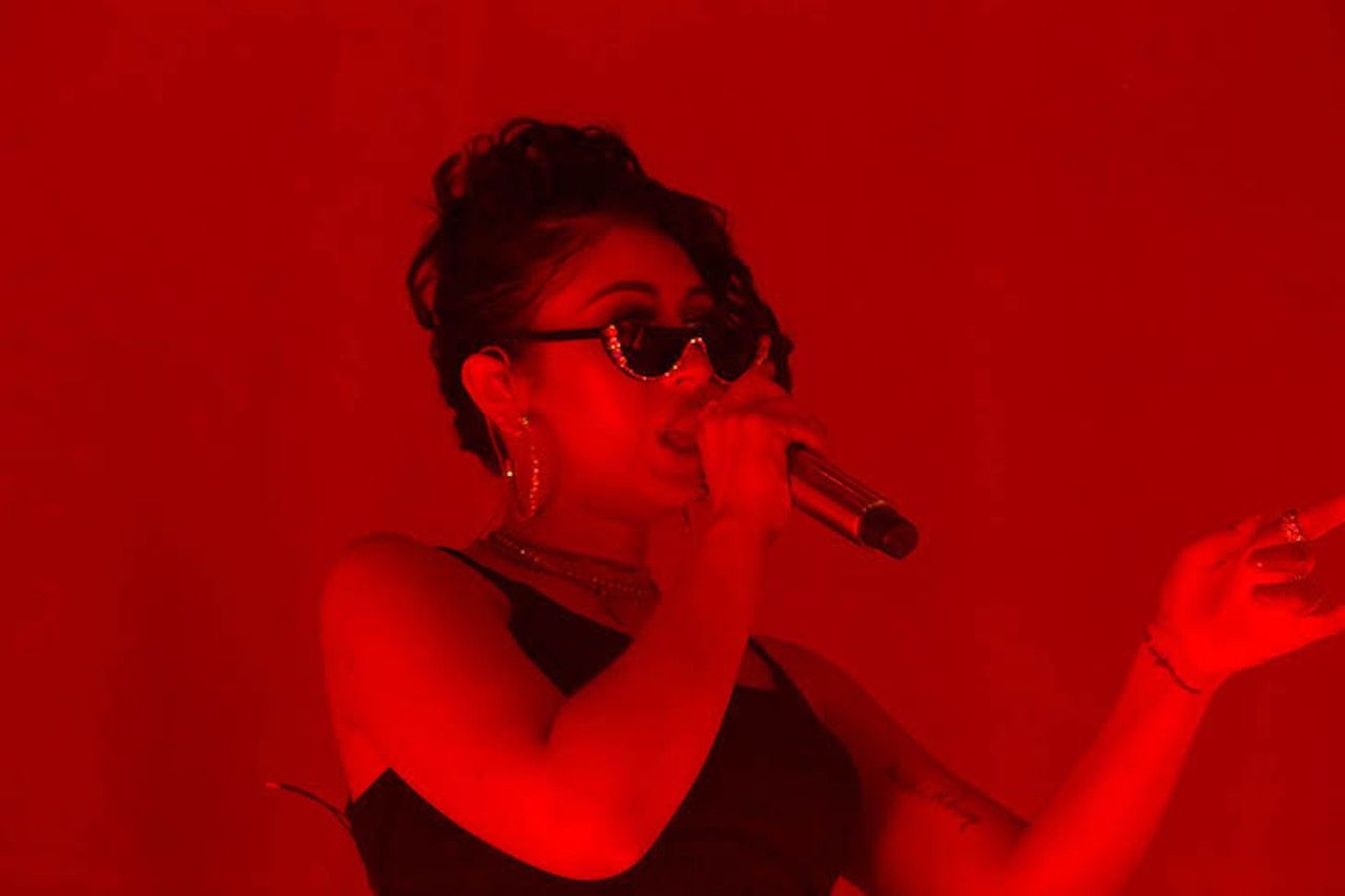 A woman singing into microphone with red light - Kali Uchis