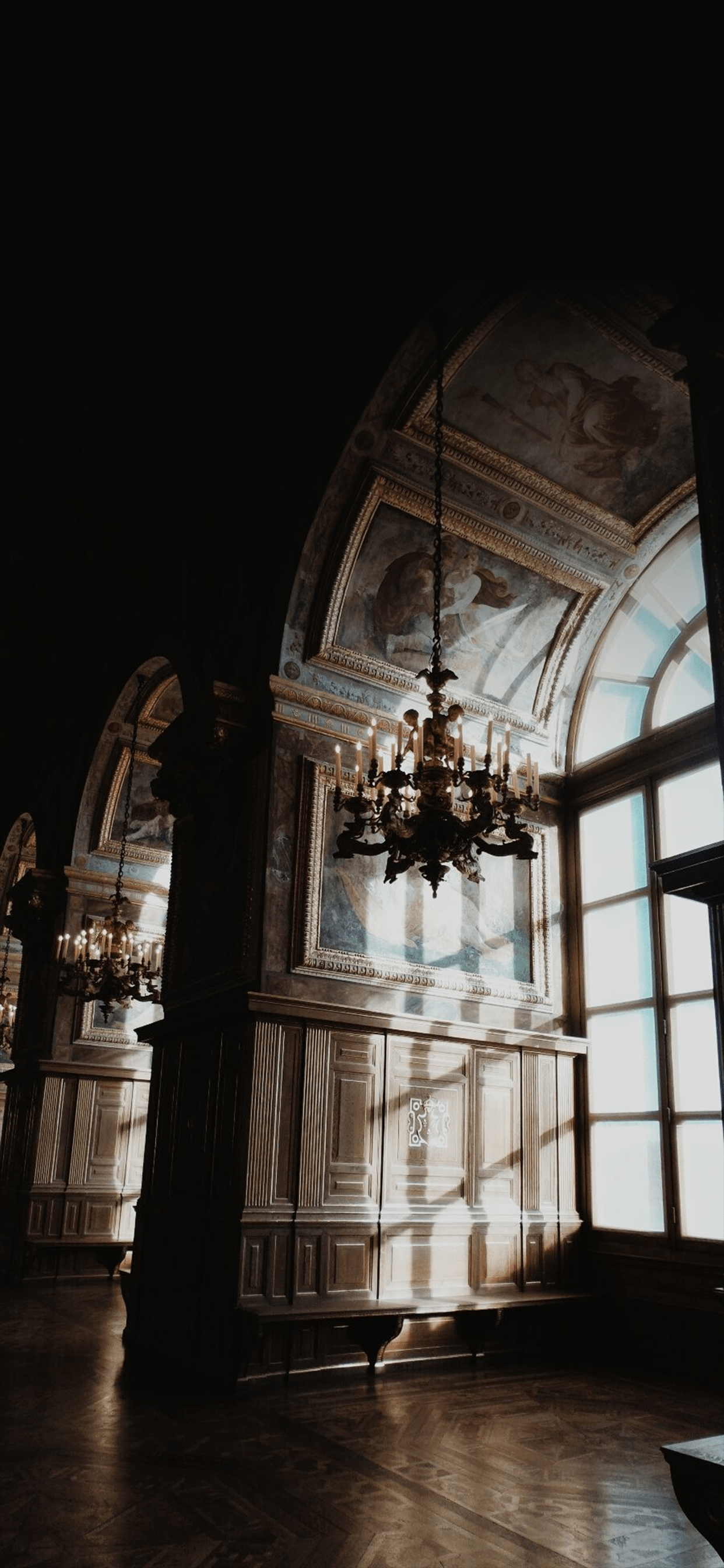 A chandelier hangs from the ceiling in a large room. - Dark academia