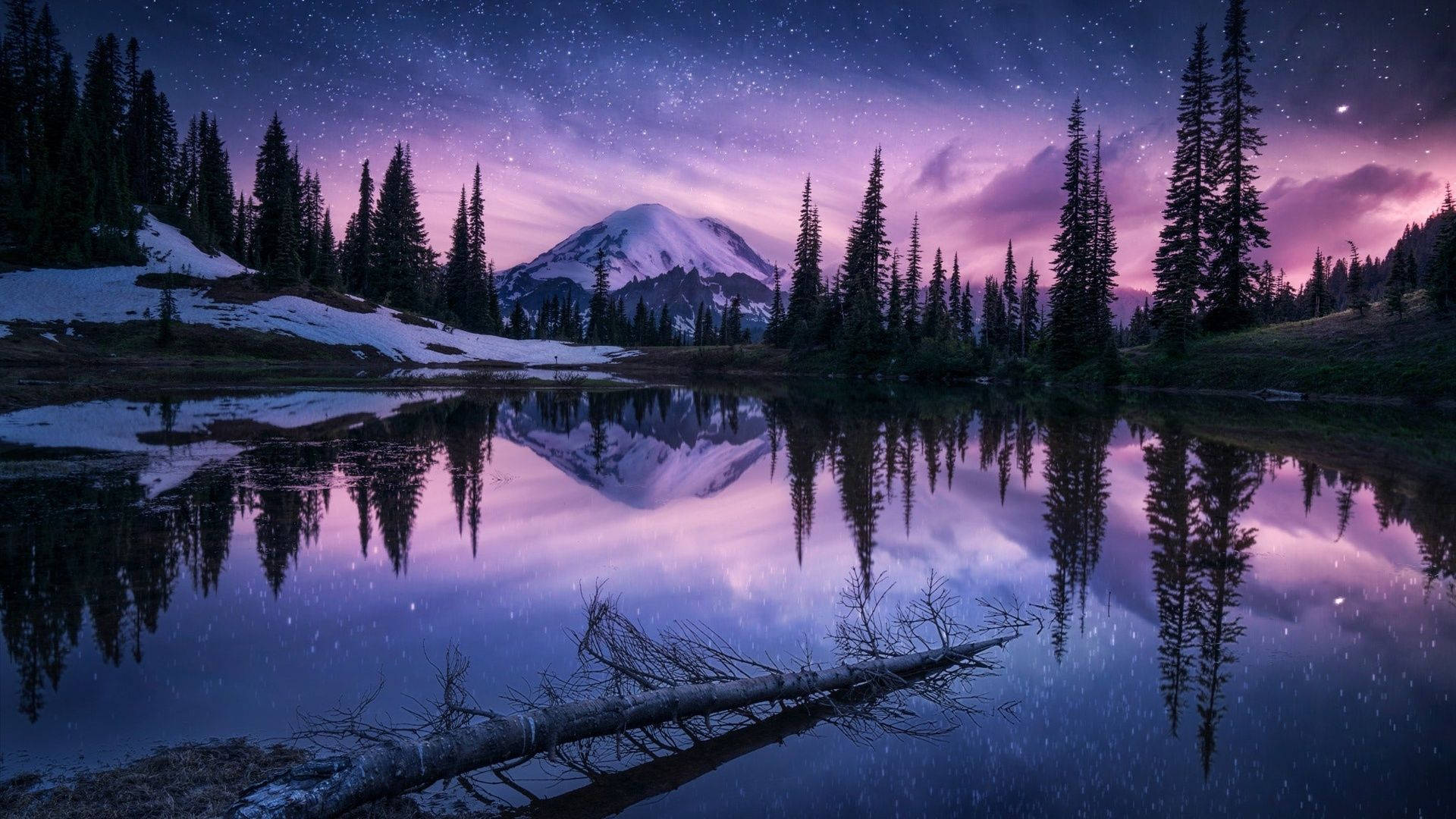 A purple and pink sky over a snow capped mountain with trees and a lake in the foreground. - Nature, lake