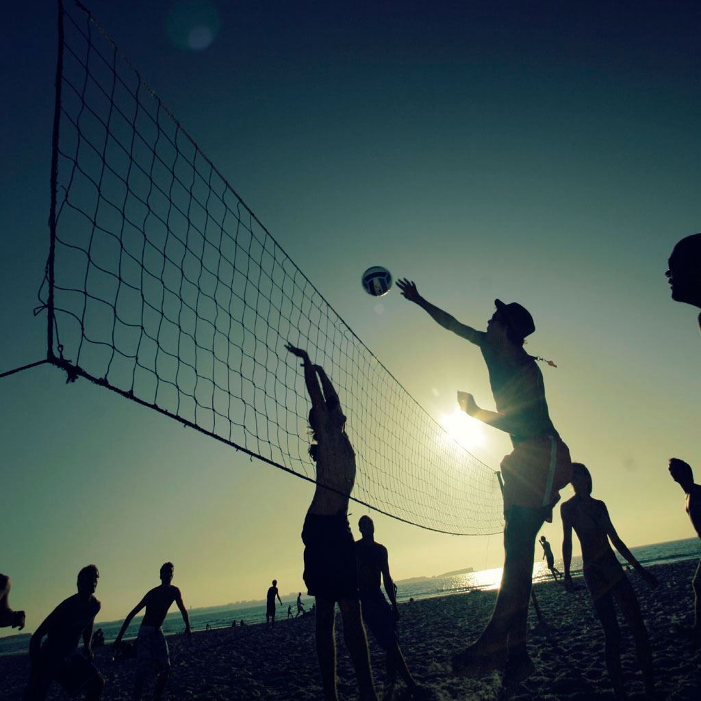 A group of people playing beach volleyball at sunset - Volleyball