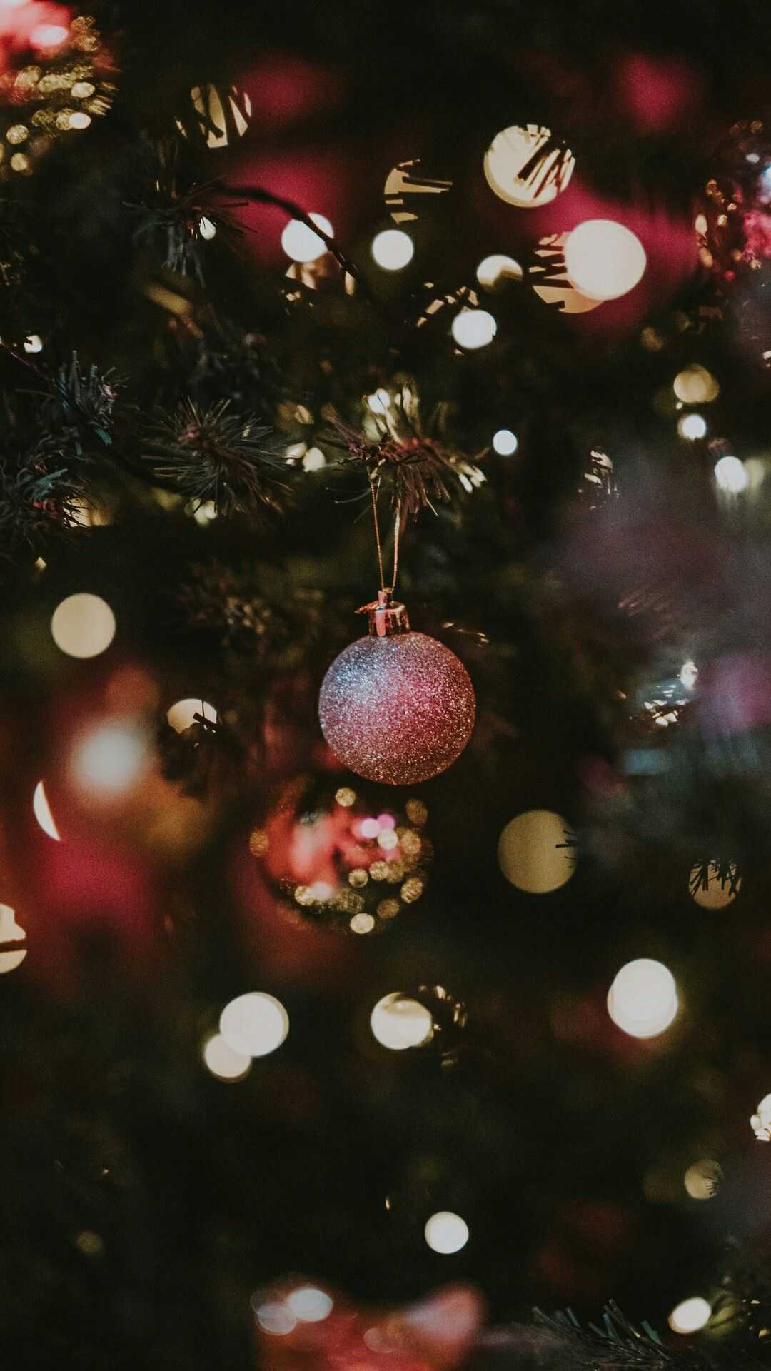 IPhone wallpaper of a Christmas tree with a red ornament hanging from it. - Christmas
