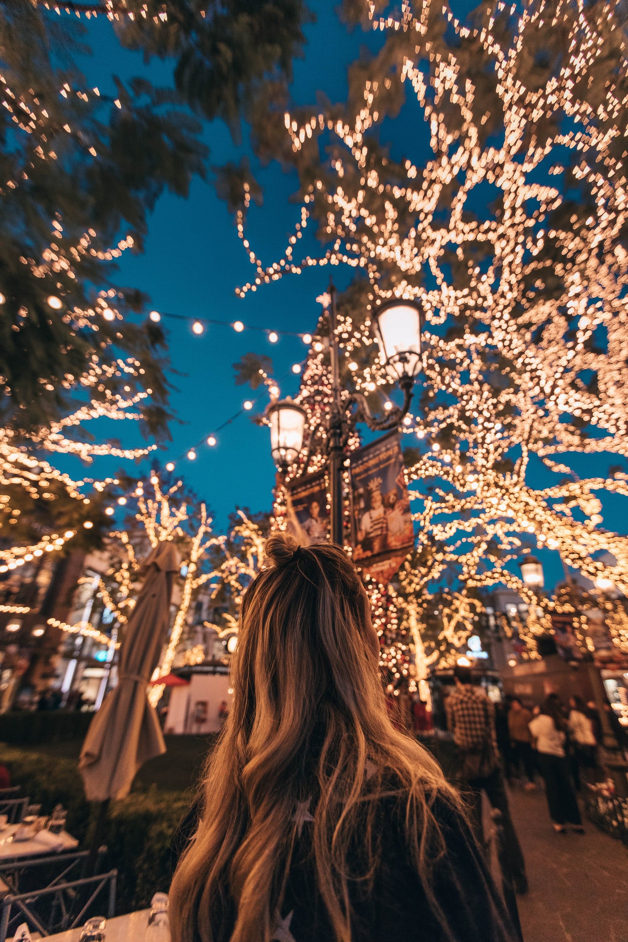 A woman with long blonde hair stands in front of a tree covered in fairy lights. - Christmas, Christmas lights