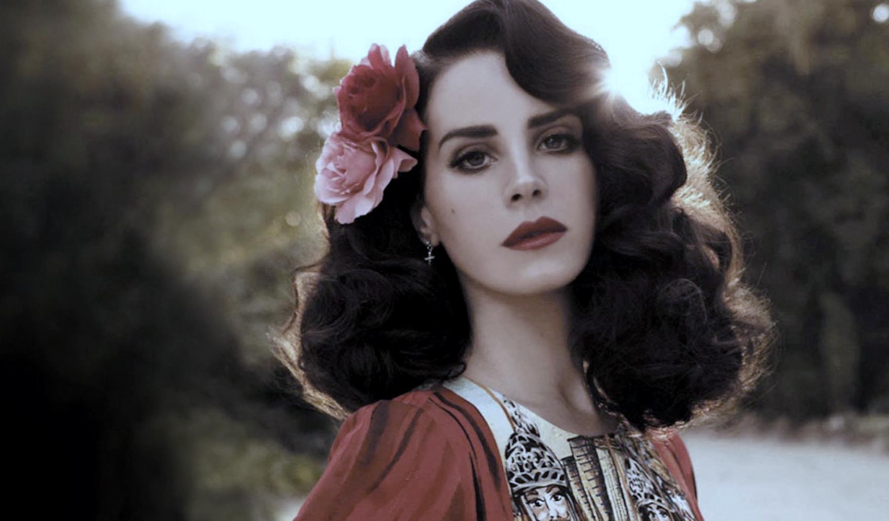 Dark haired woman with a flower in her hair and red lipstick - Lana Del Rey