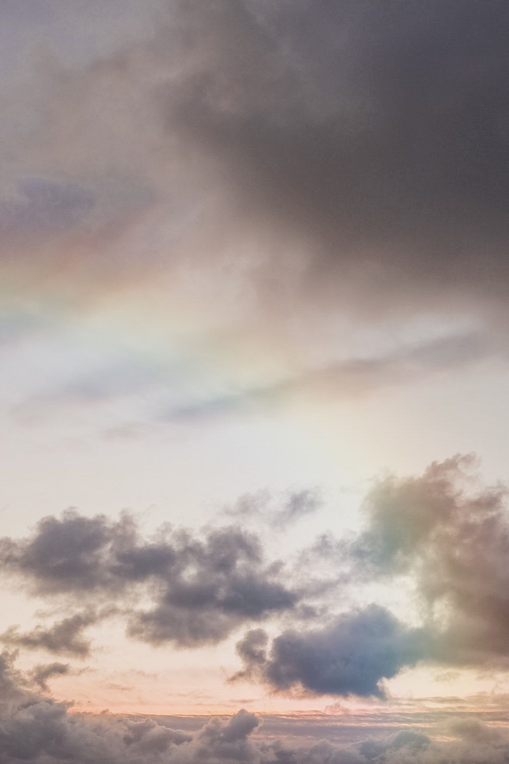 A rainbow appears in the sky above the clouds. - Pastel rainbow