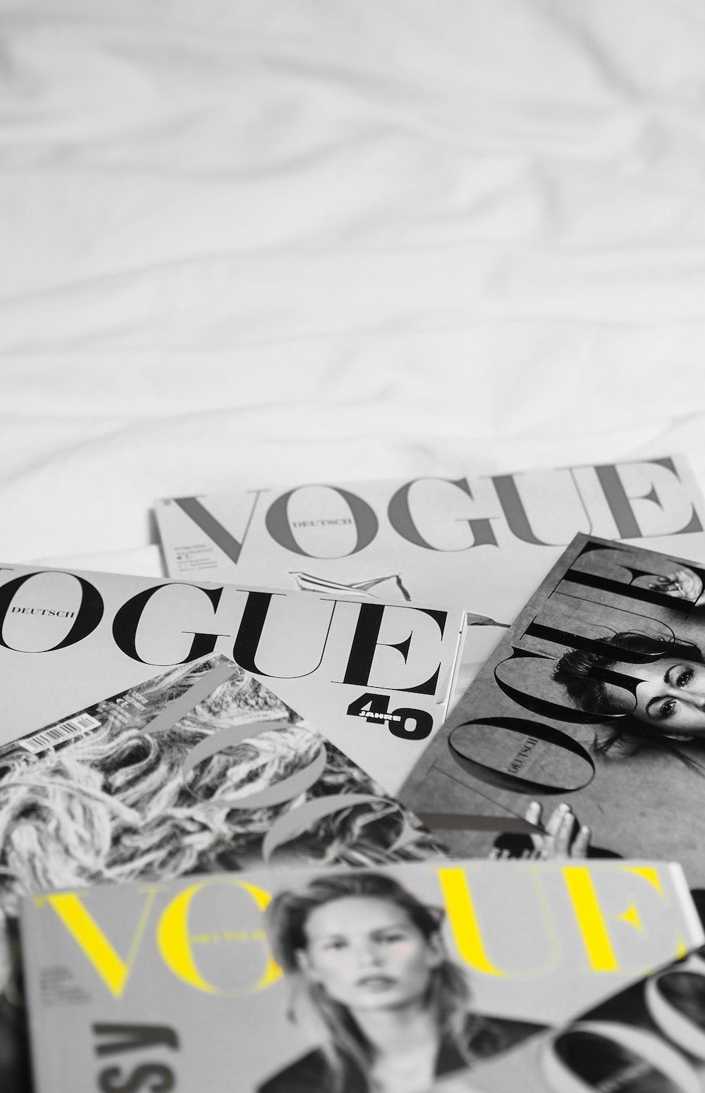 A black and white photo of a pile of Vogue magazines on a bed. - Vogue