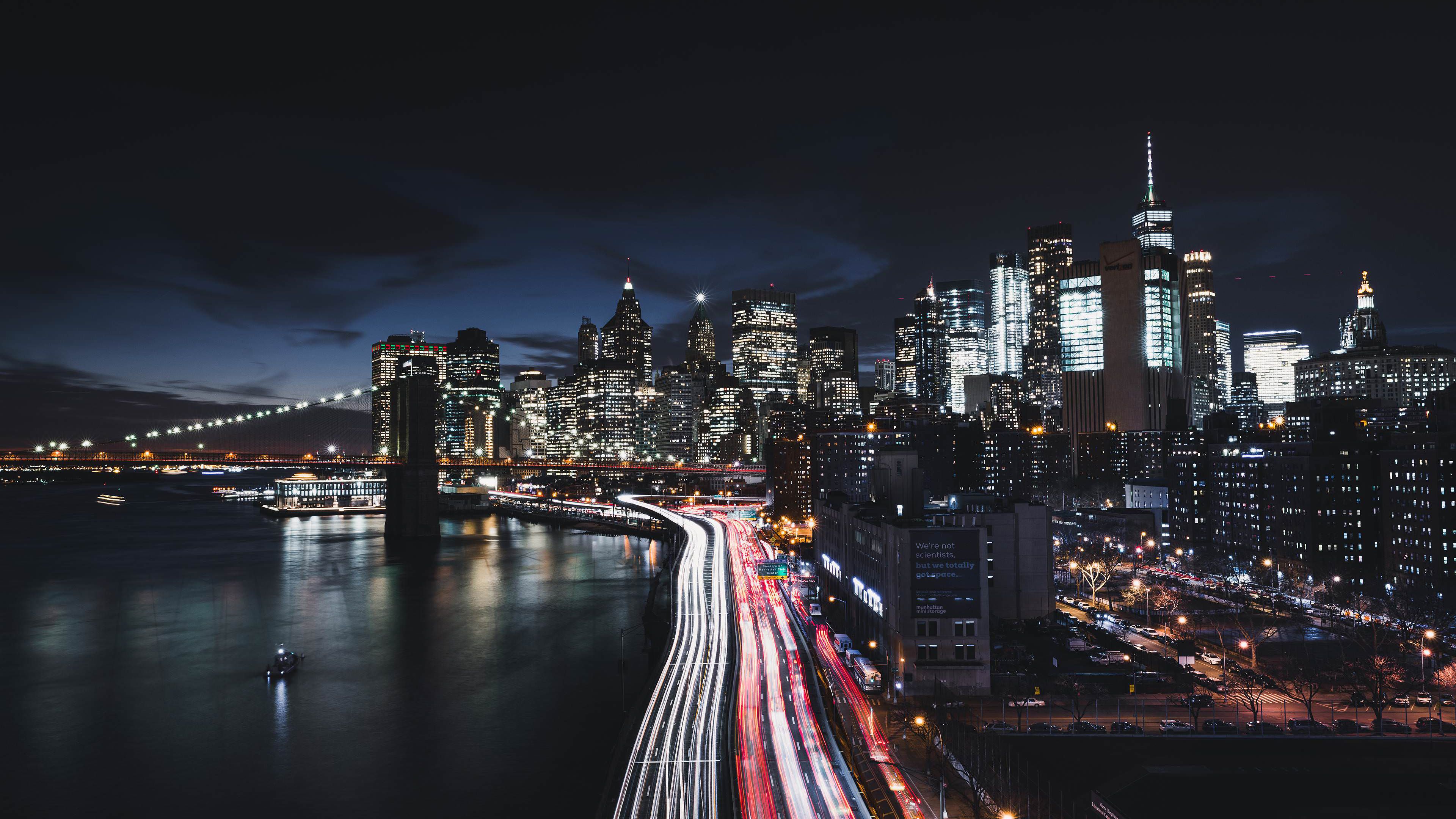 A city skyline at night with a river and bridge in the foreground. - New York