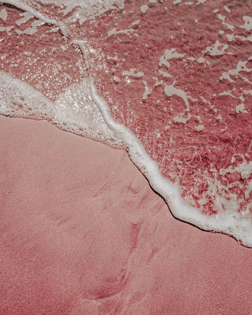 A pink sand beach with white sea foam. - Hot pink