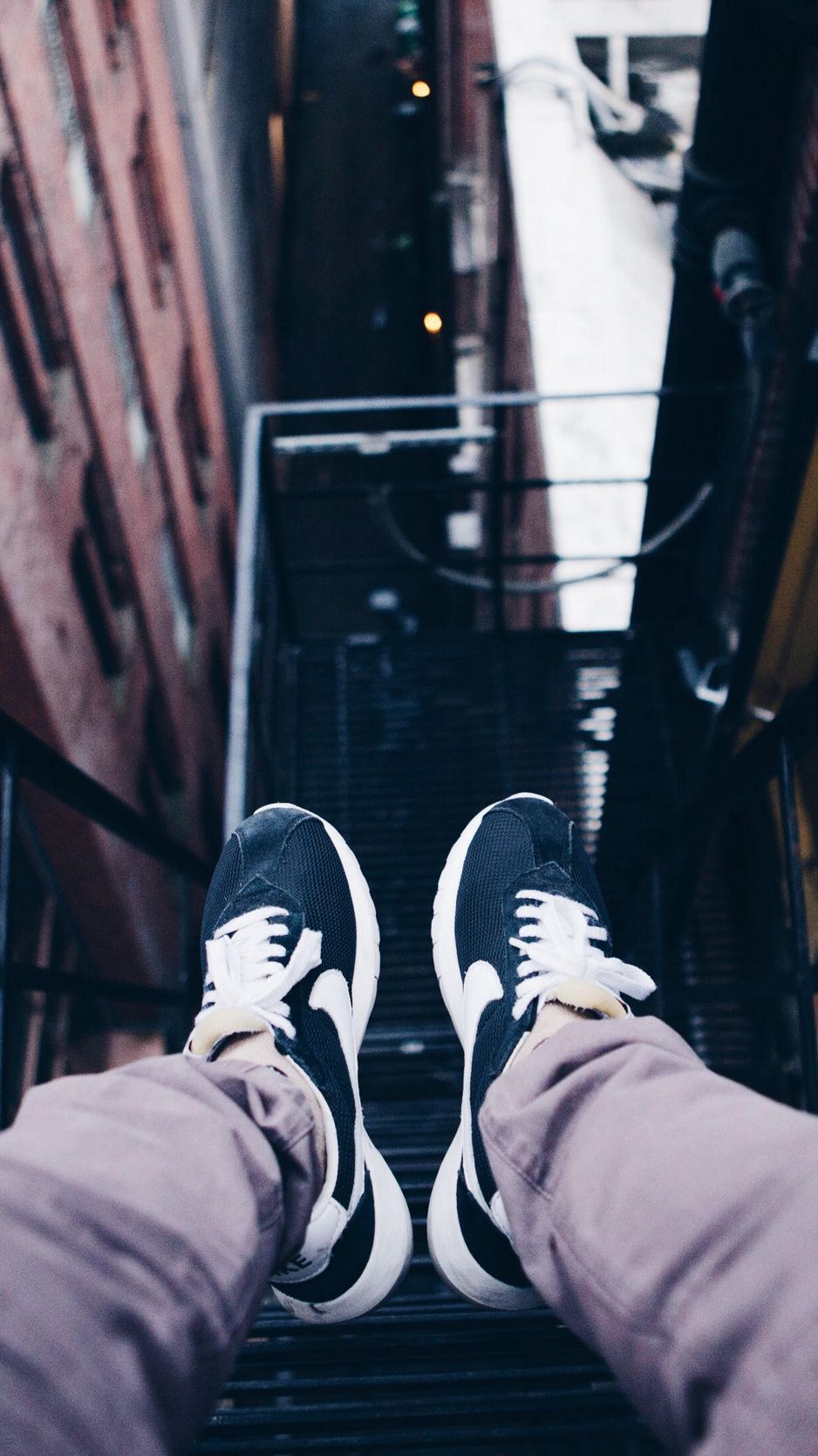 A person wearing black and white sneakers is standing on a metal staircase. - Shoes