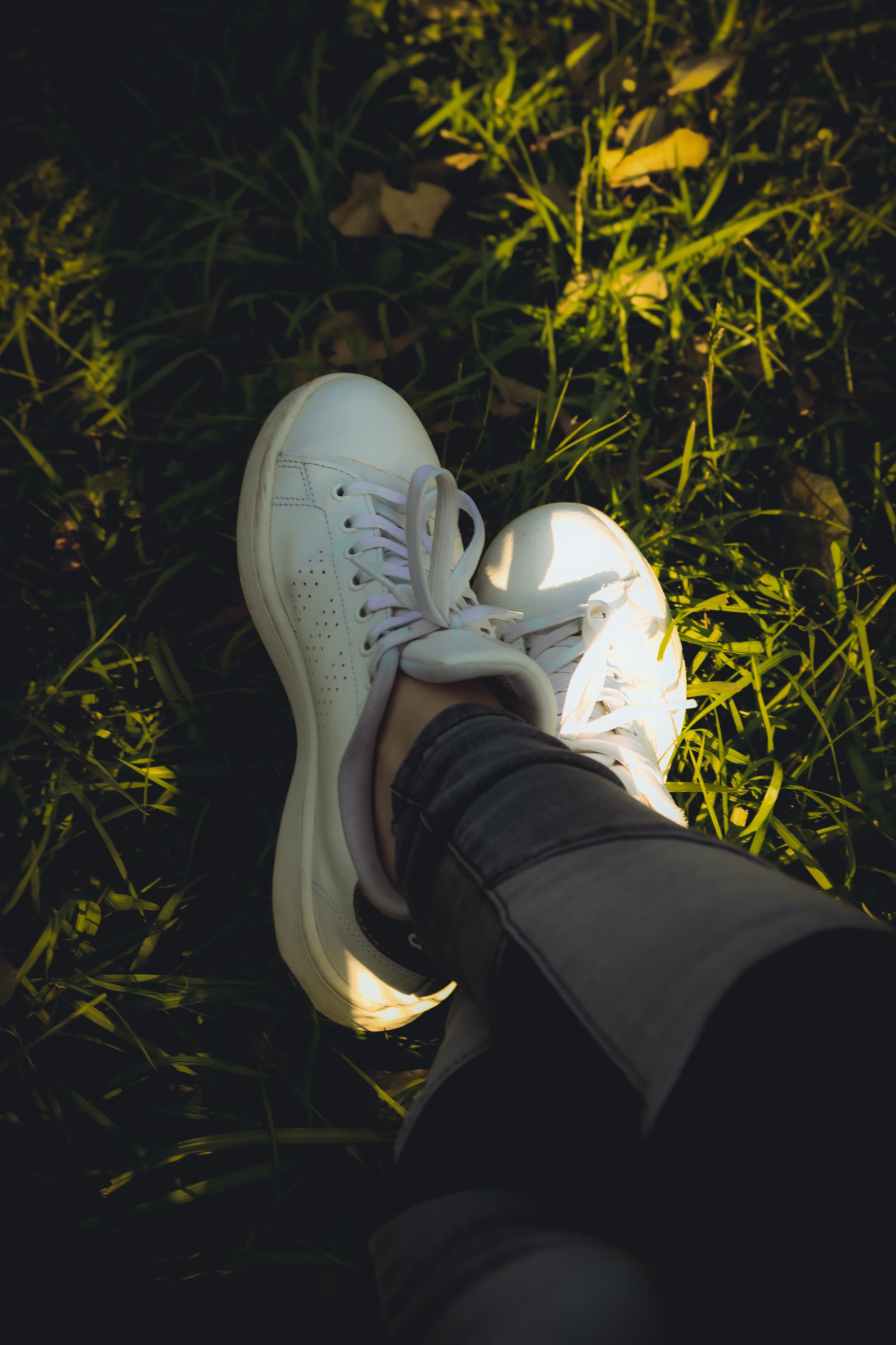 A pair of feet wearing white sneakers standing on grass. - Shoes