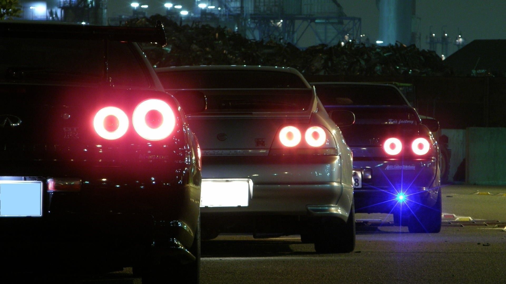 A row of cars with their lights on at night. - JDM