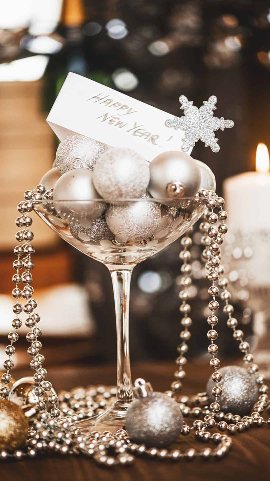 A champagne glass filled with silver Christmas ornaments and a card that says 