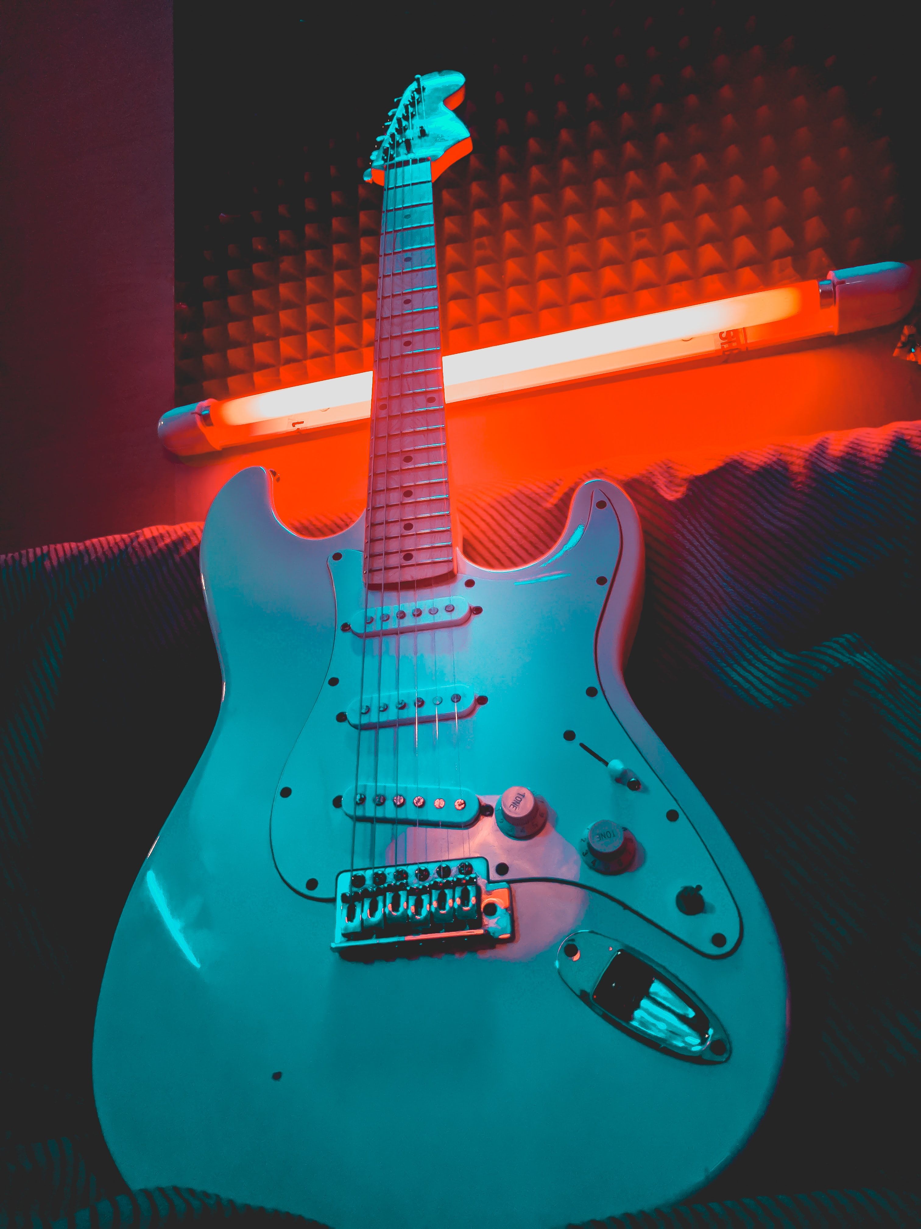 A white electric guitar with a red and blue neon light behind it. - Guitar