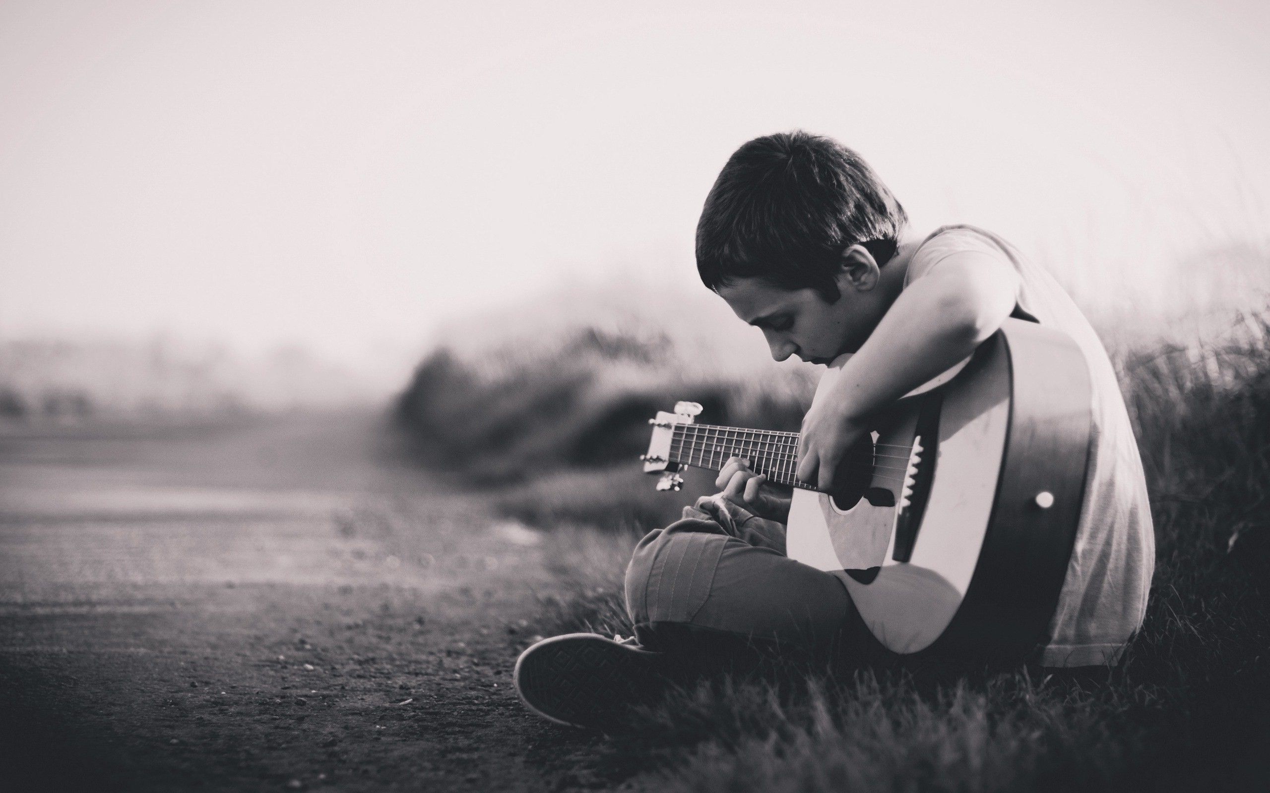 A boy playing guitar on the side of road - Guitar