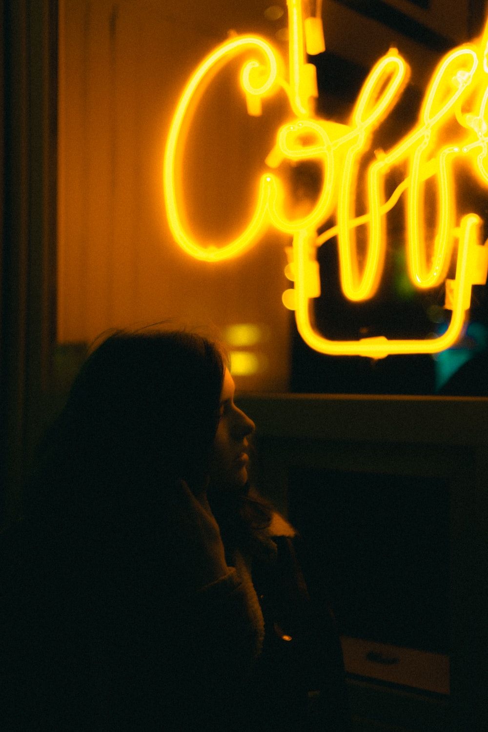 woman in gray hoodie standing near red and yellow neon light signage photo