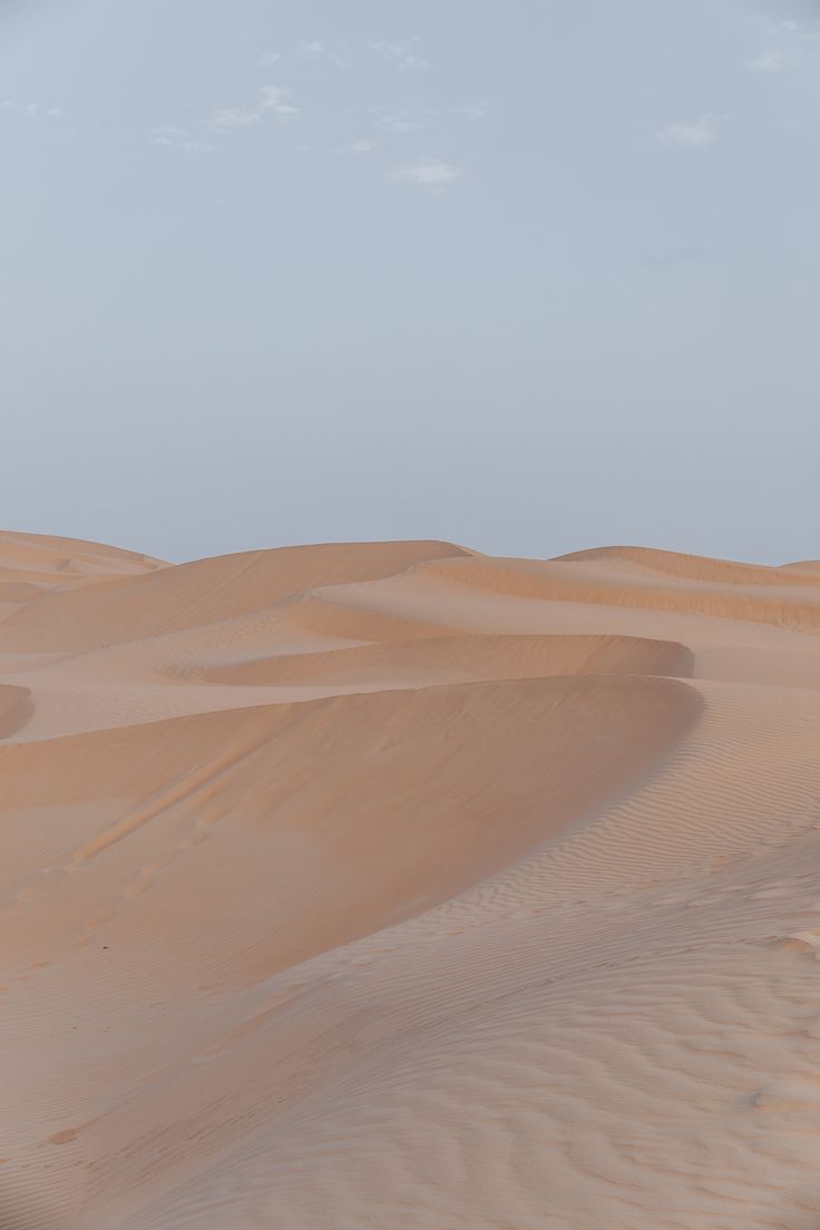 Sand dunes in the desert with a hazy blue sky above. - Desert