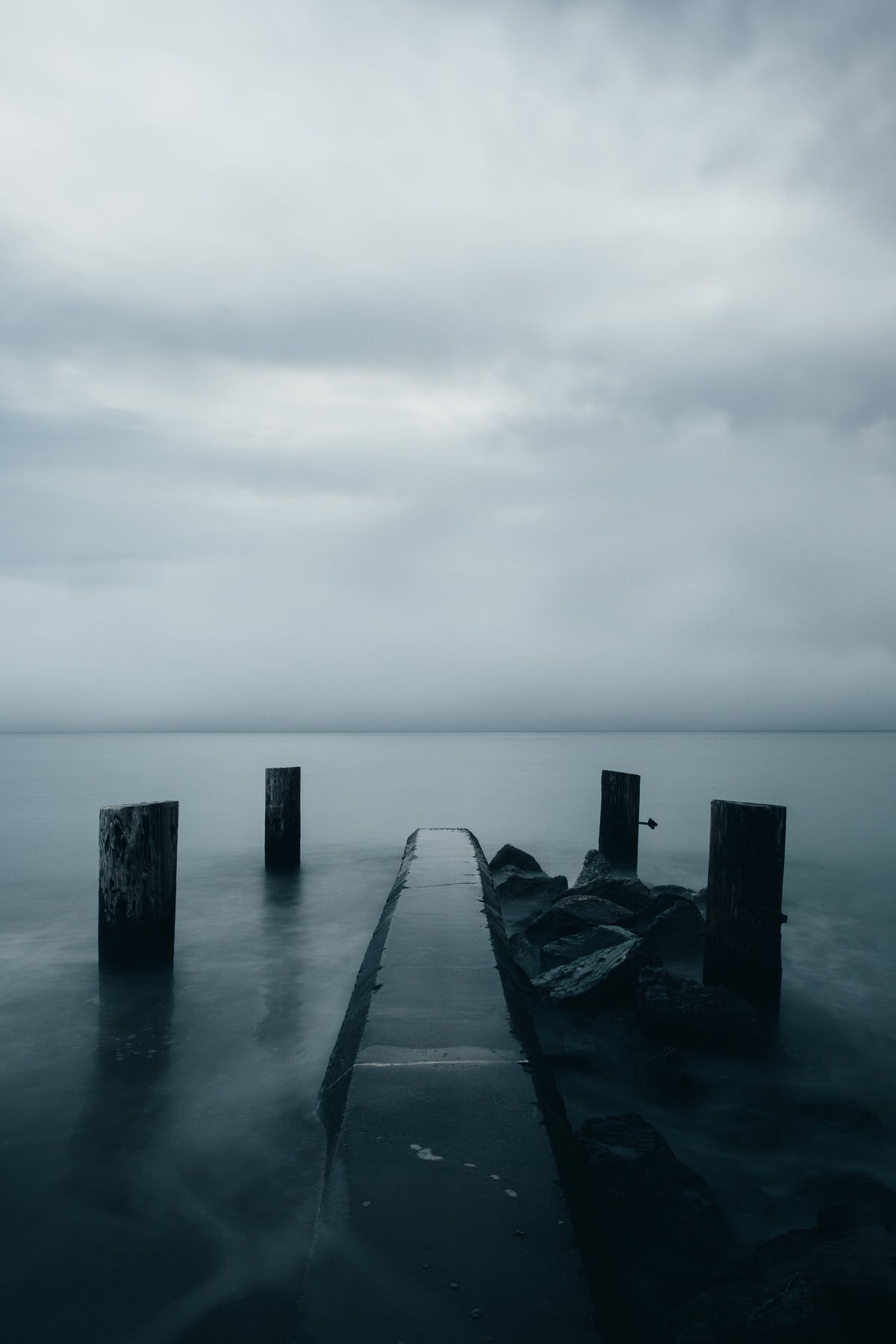 A pier leading out into a body of water on a cloudy day. - Magic