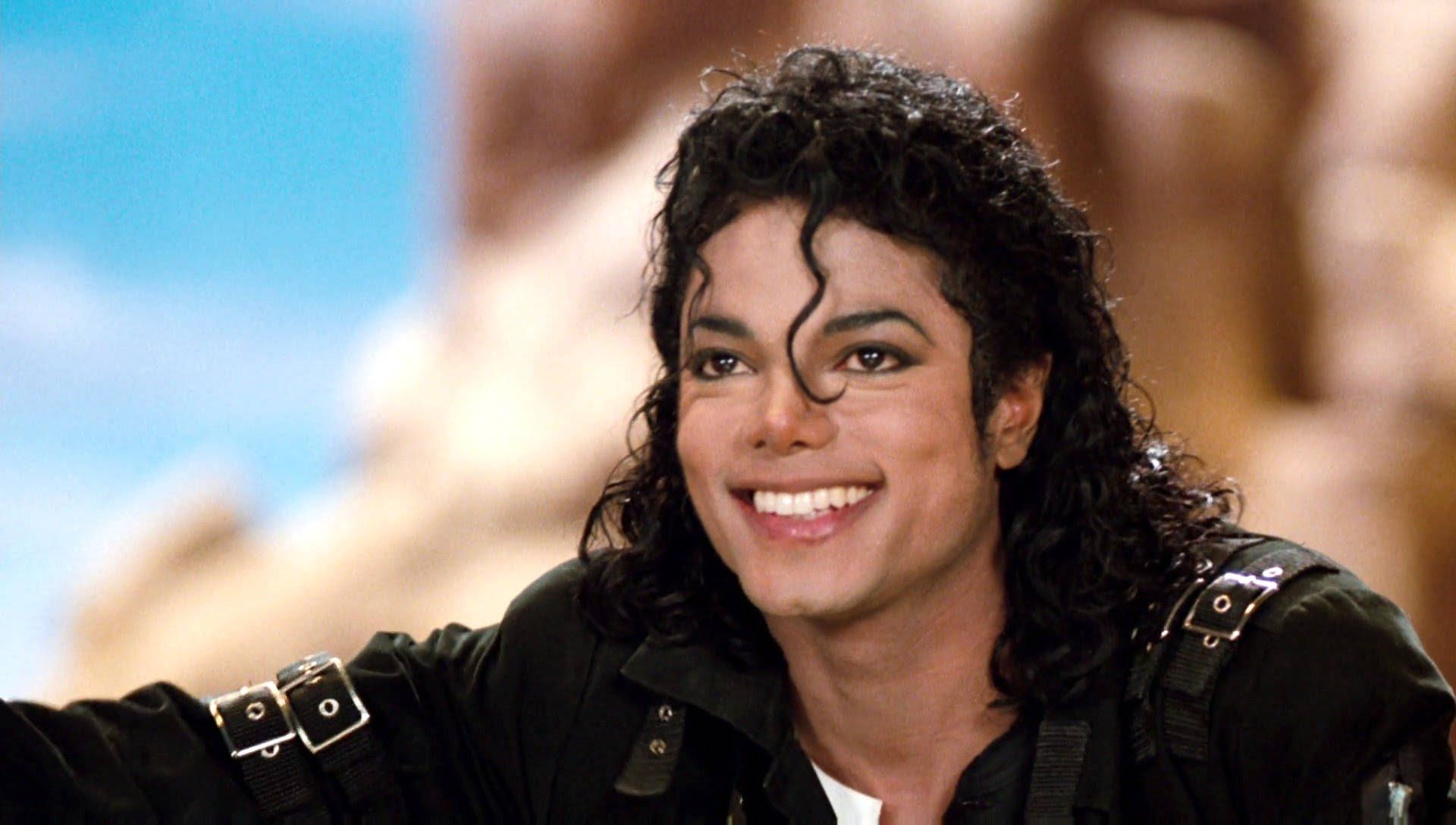 Michael Jackson is smiling and wearing a black jacket. - Michael Jackson