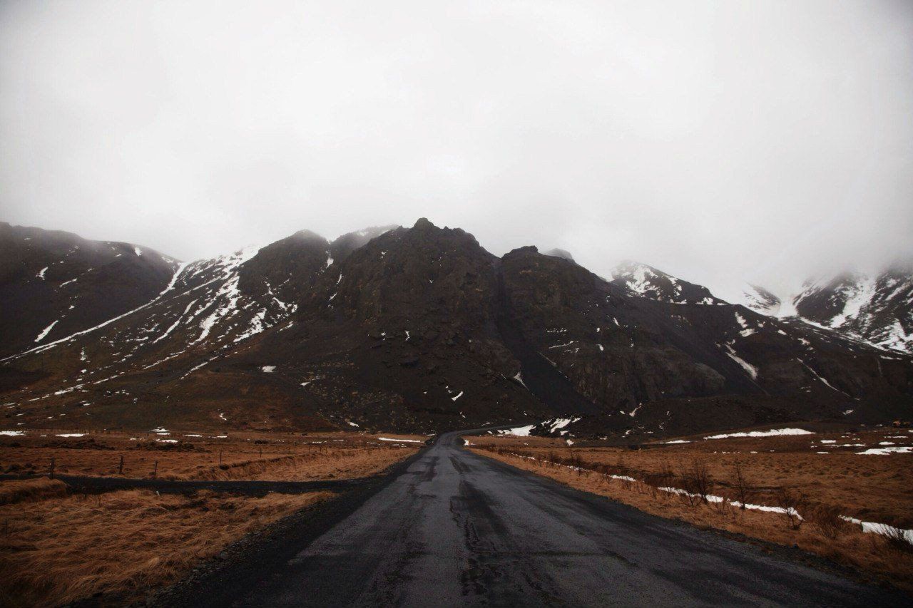 A long road stretches out in front of a snow-covered mountain. - Road