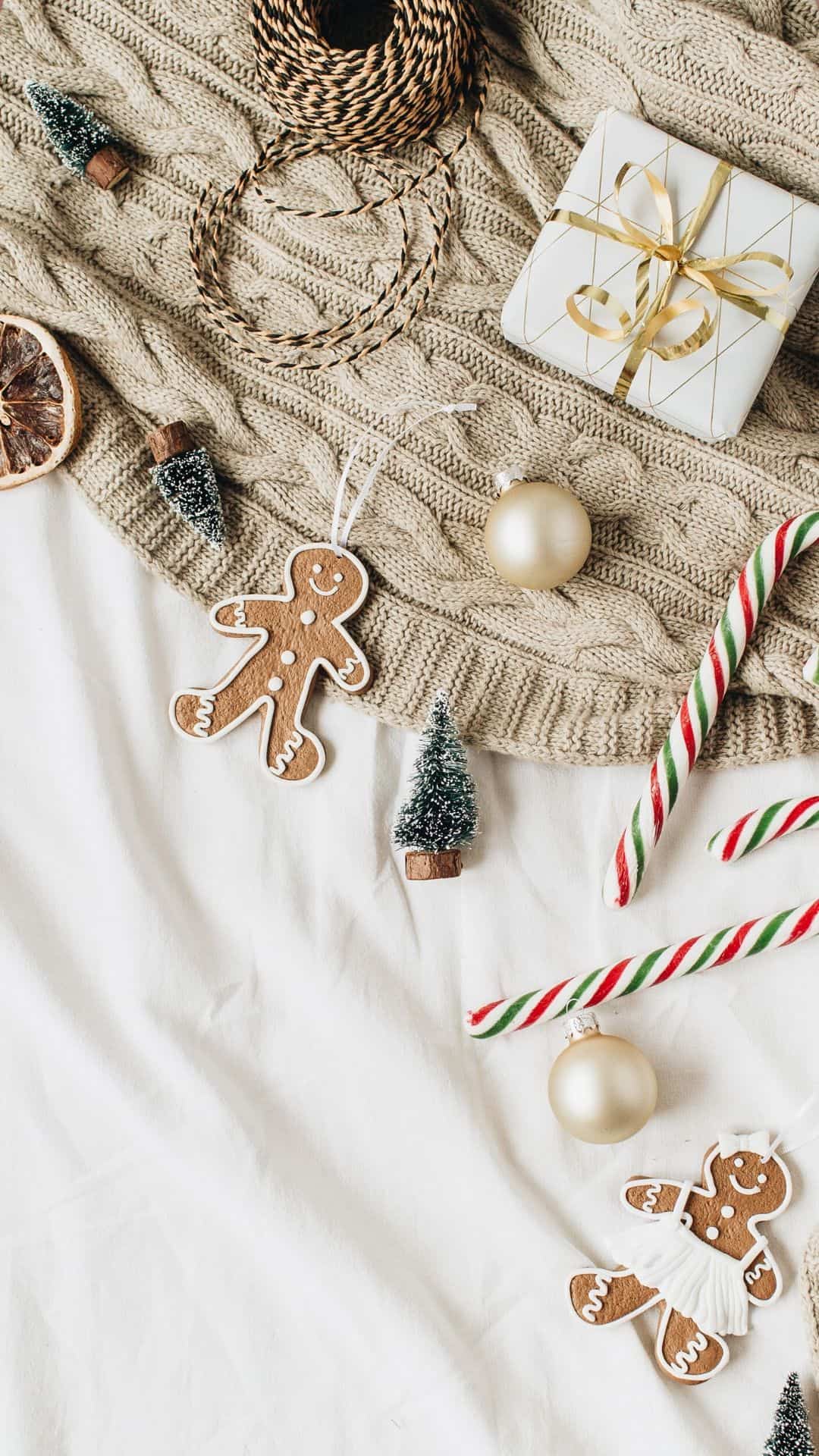A flat lay of a beige knitted sweater, candy canes, gingerbread men, and Christmas ornaments. - Cozy