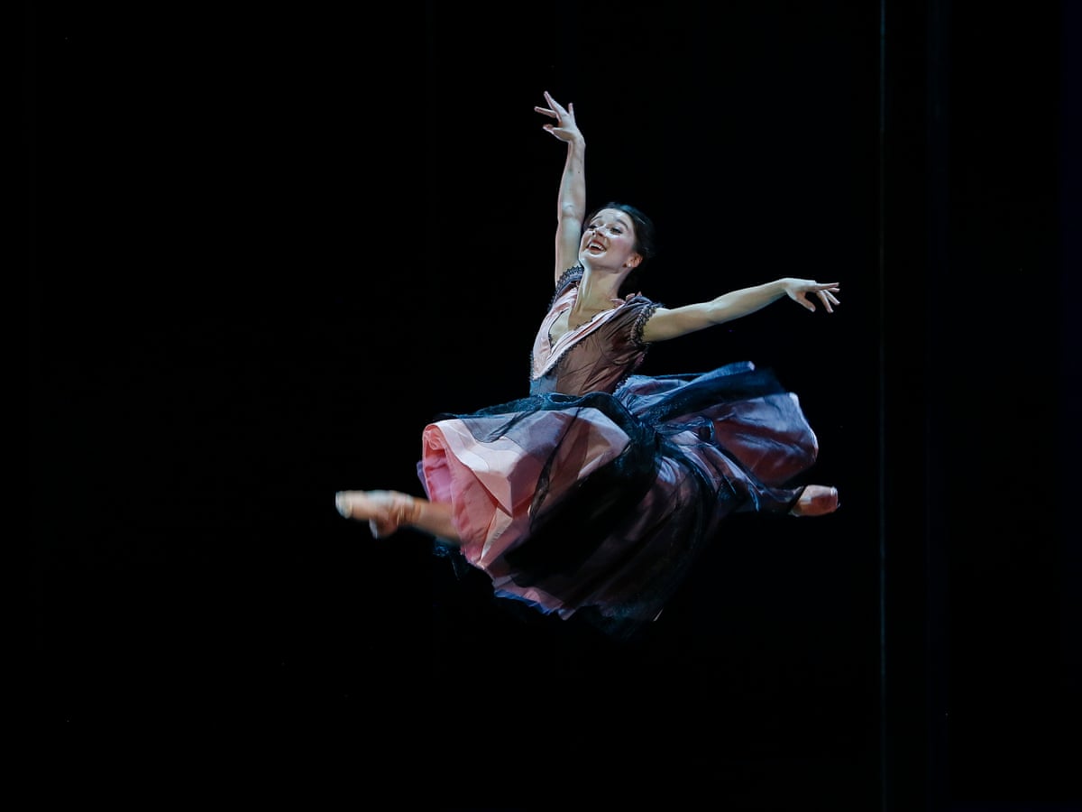 A ballerina in a pink and blue dress leaps into the air with her arms outstretched. - Ballet