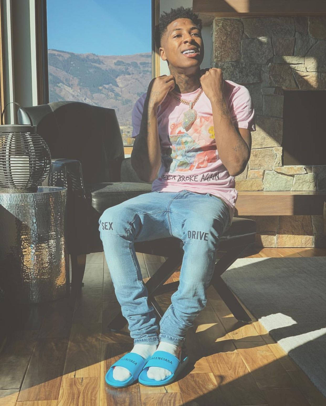 NBA YoungBoy is seen wearing a pink t-shirt and light blue jeans. - 