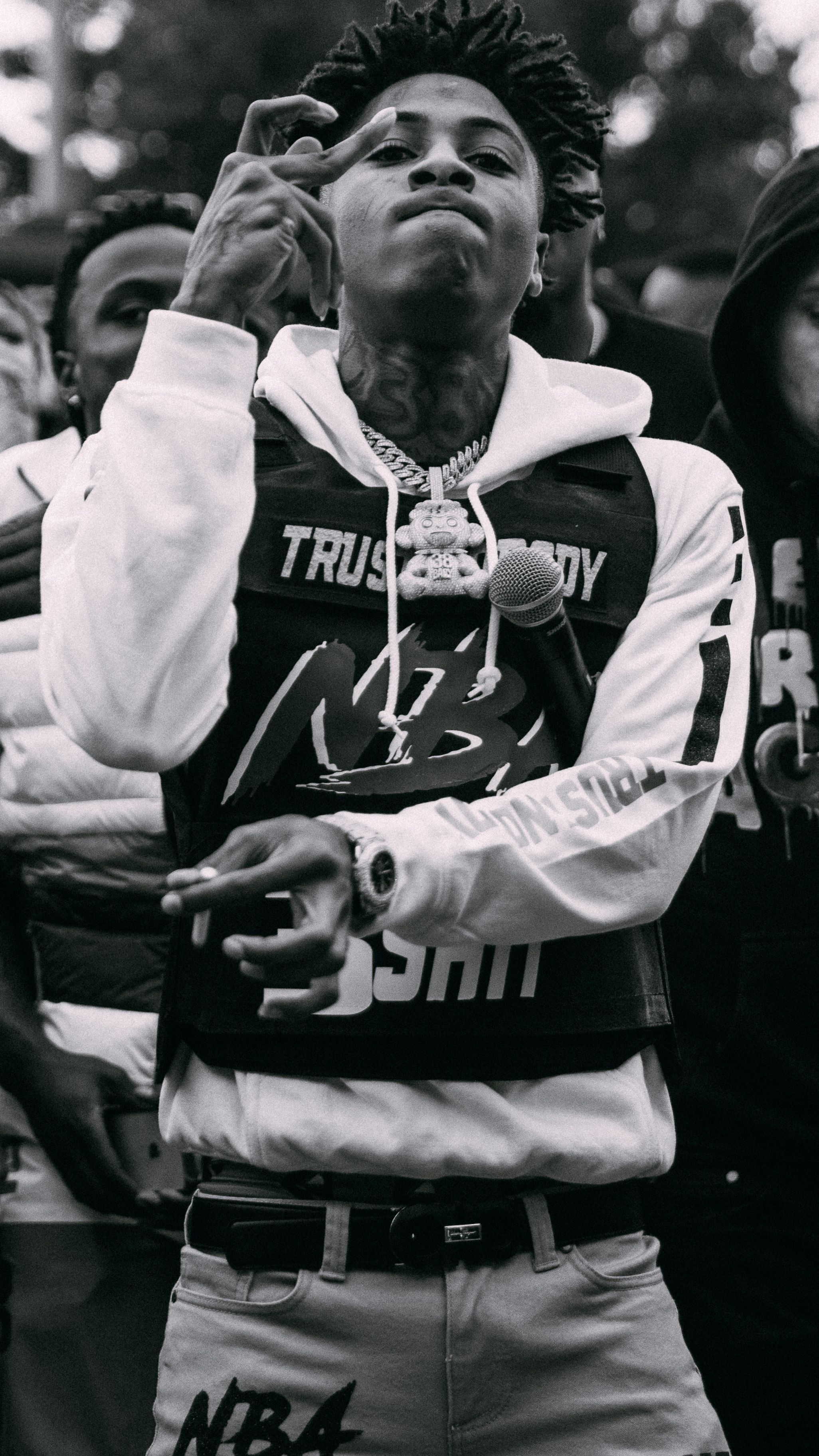 A black and white photo of NBA YoungBoy holding a microphone and making a hand gesture - NBA