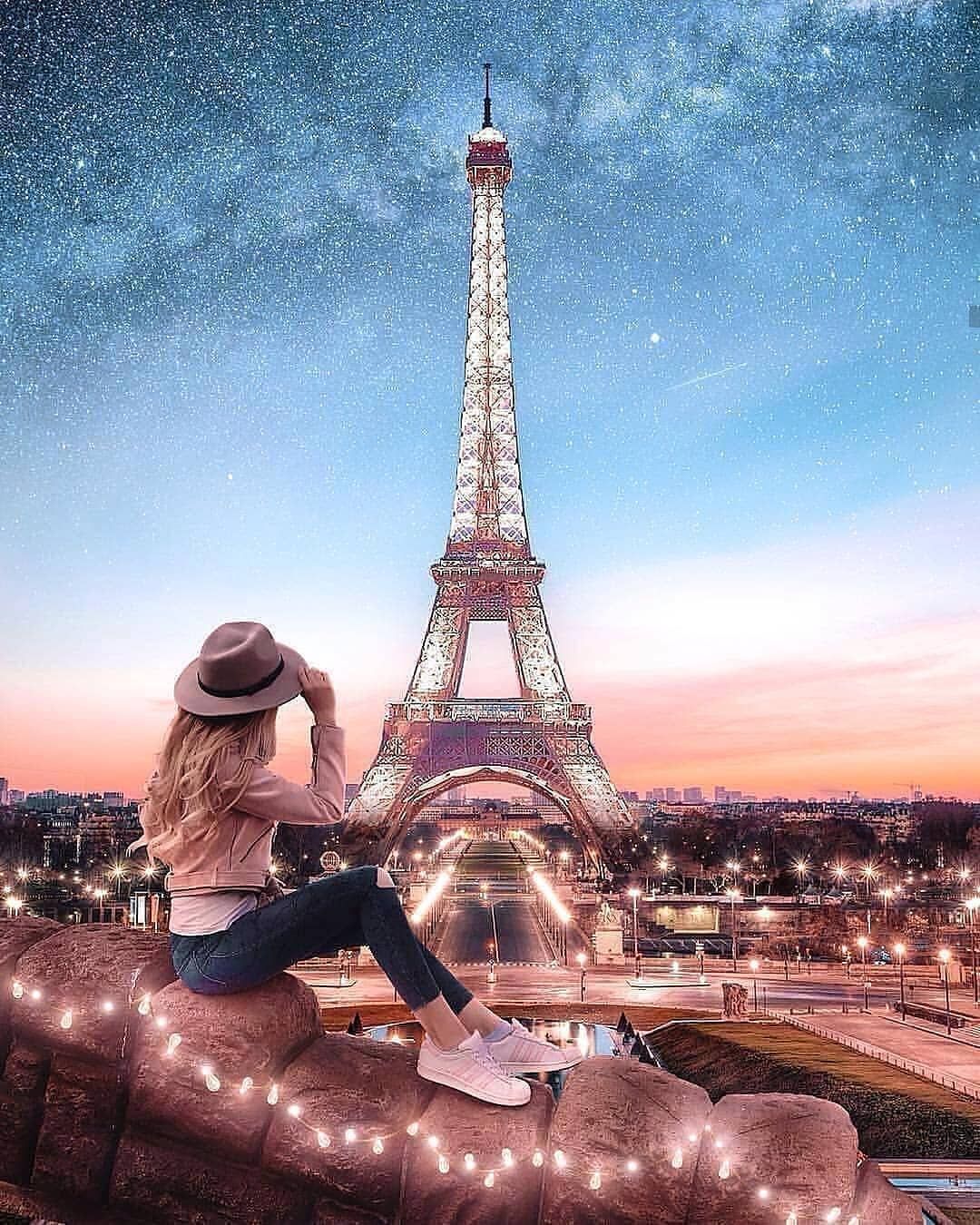 A woman sitting on the edge of something looking at an eiffel tower - Paris