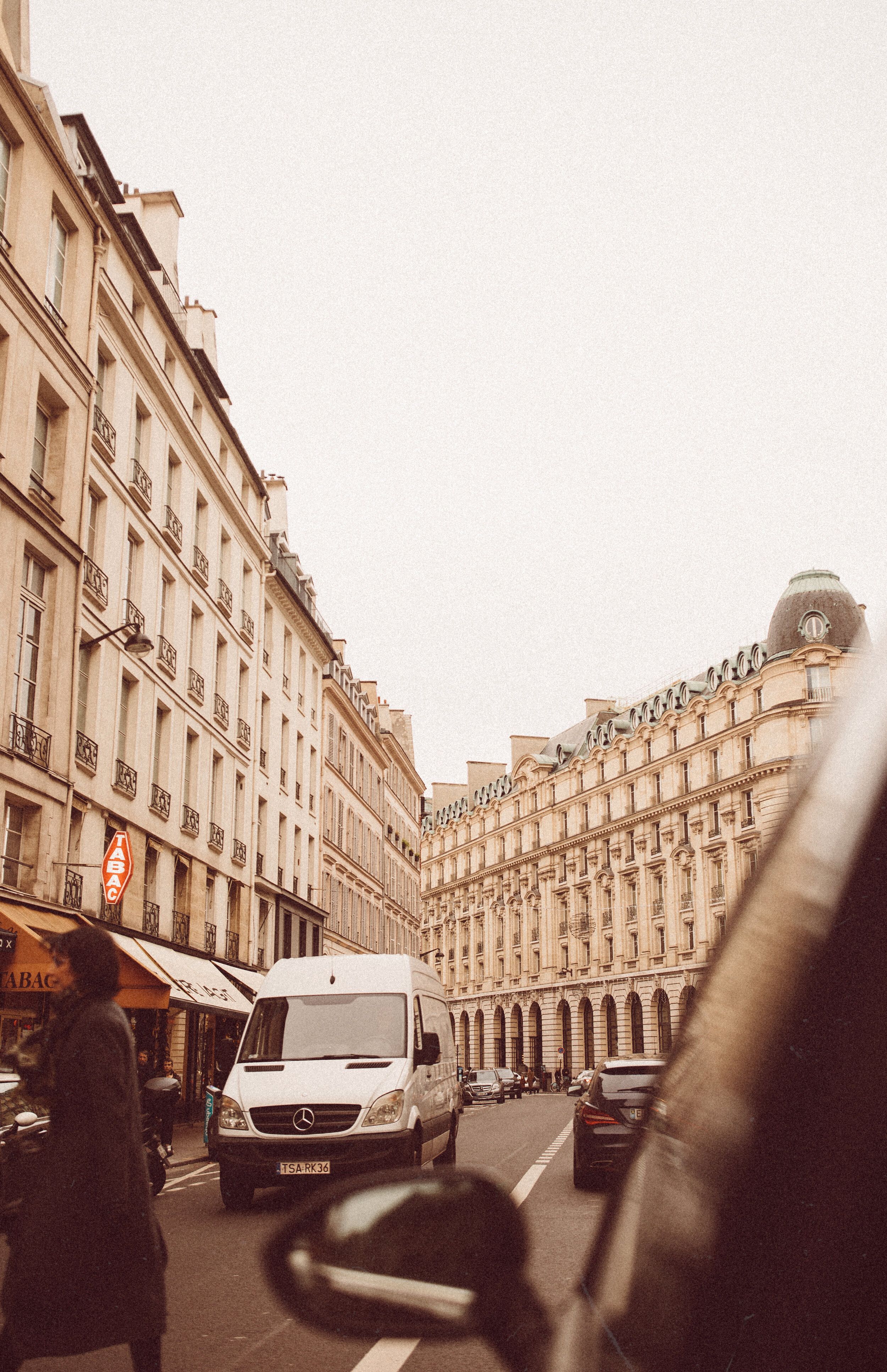 A van driving down a busy city street with buildings on both sides of the street. - Paris