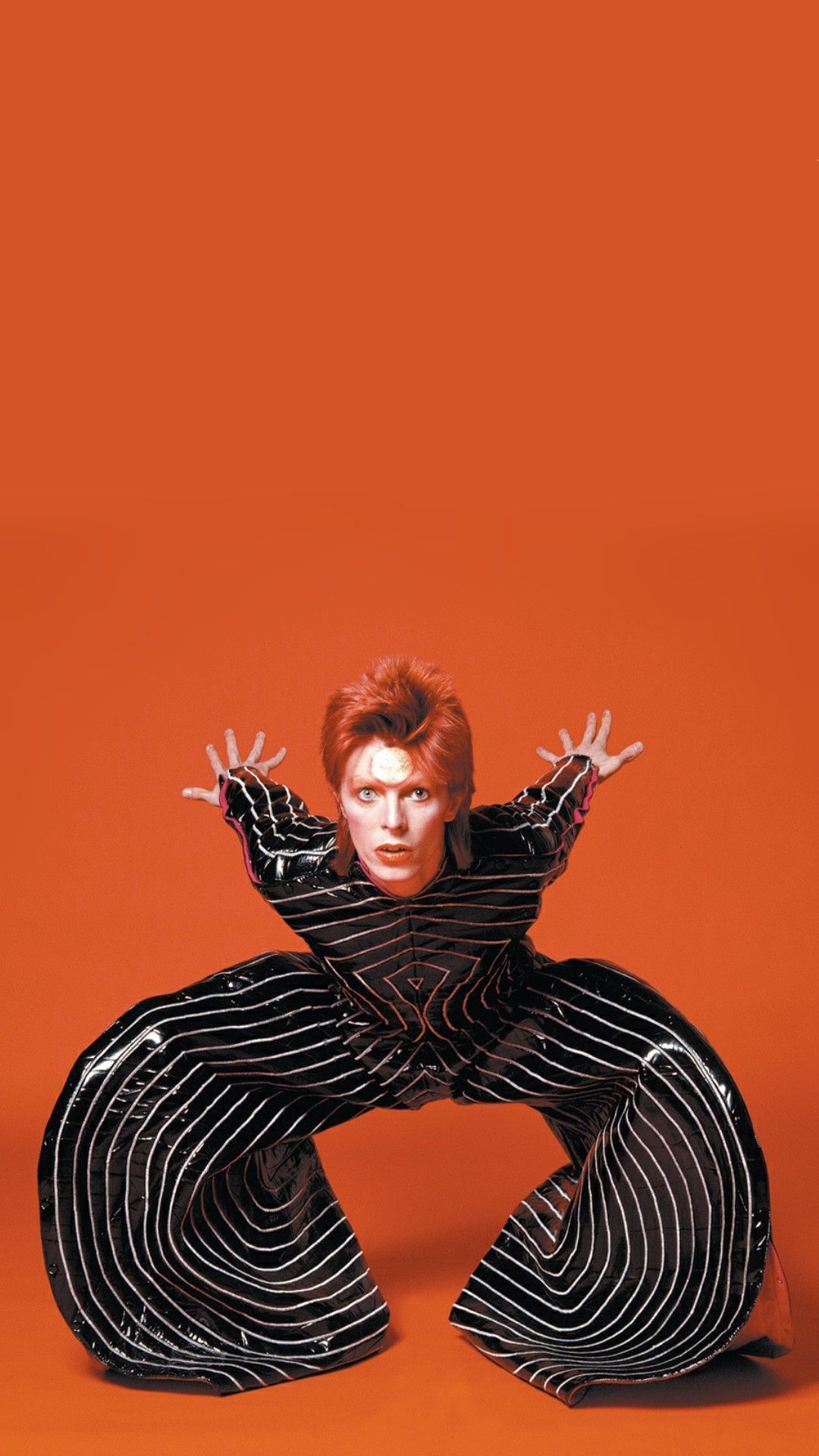 David Bowie in his Ziggy Stardust outfit, with his hands outstretched and legs bent in a wide V shape - David Bowie