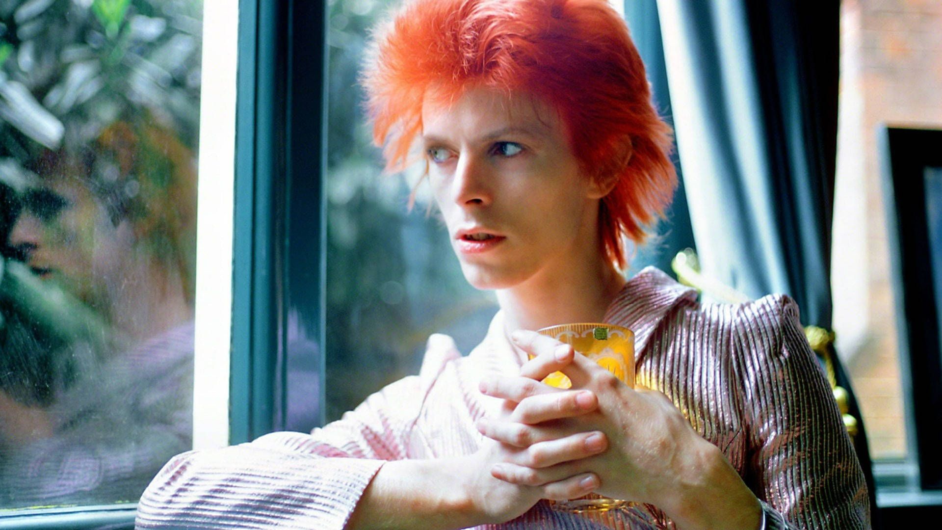 David Bowie, holding a glass of orange juice, looking out the window - David Bowie