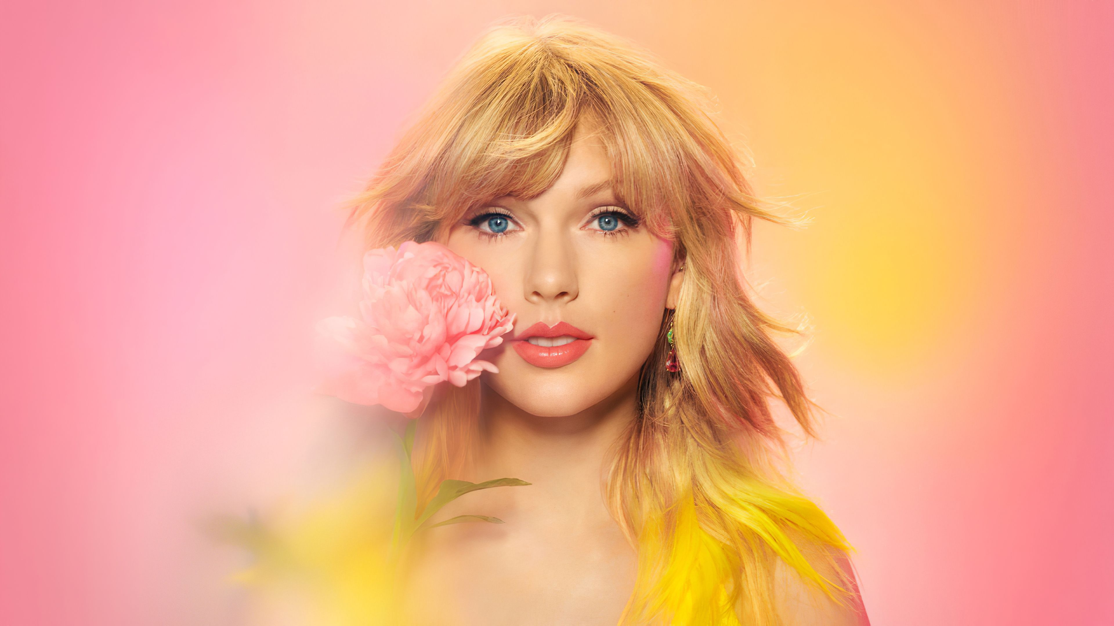 A blonde woman with bangs holding a pink flower to her face - Taylor Swift