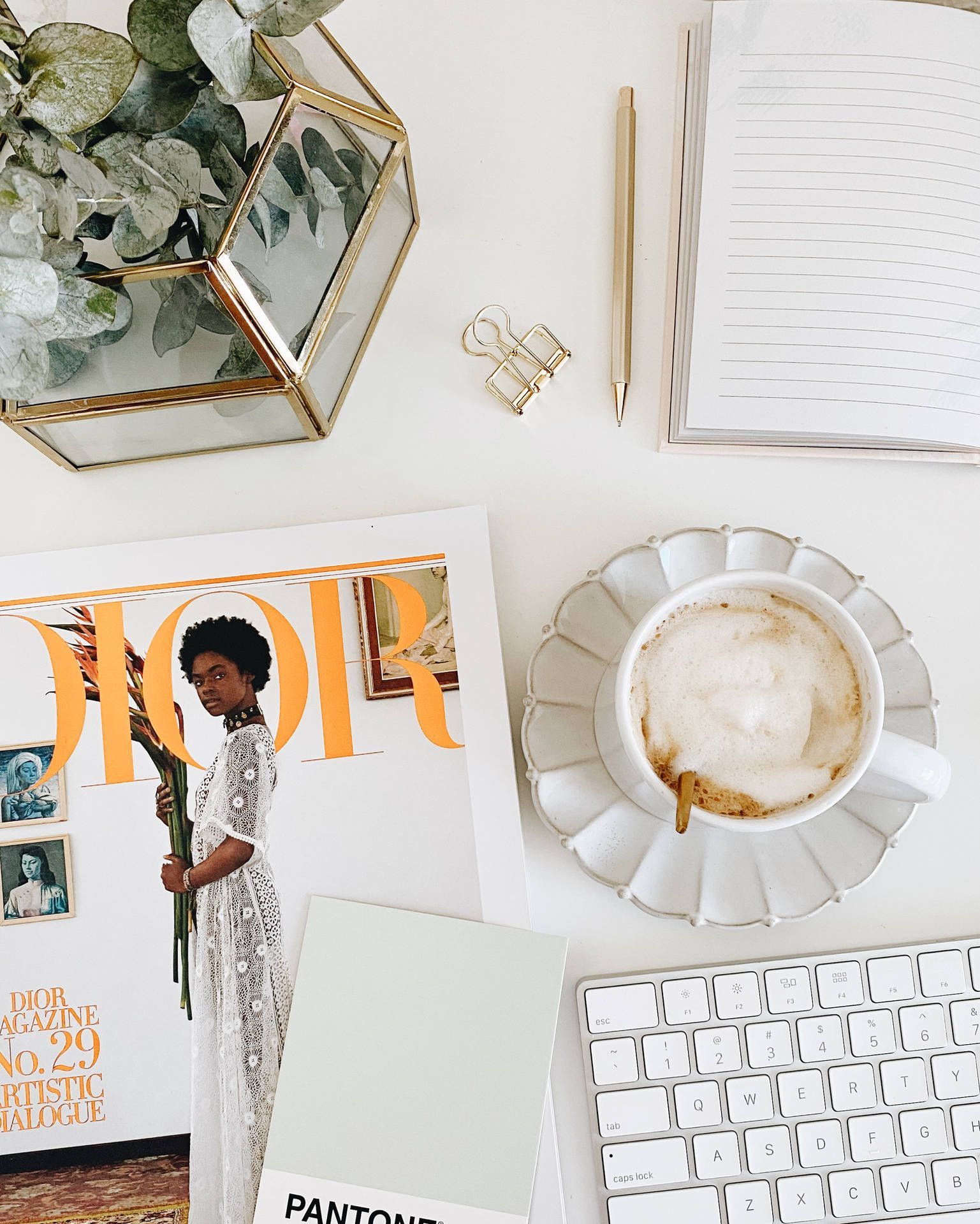 A flat lay of a desk with a keyboard, mouse, open book, and a Dior magazine. - Dior