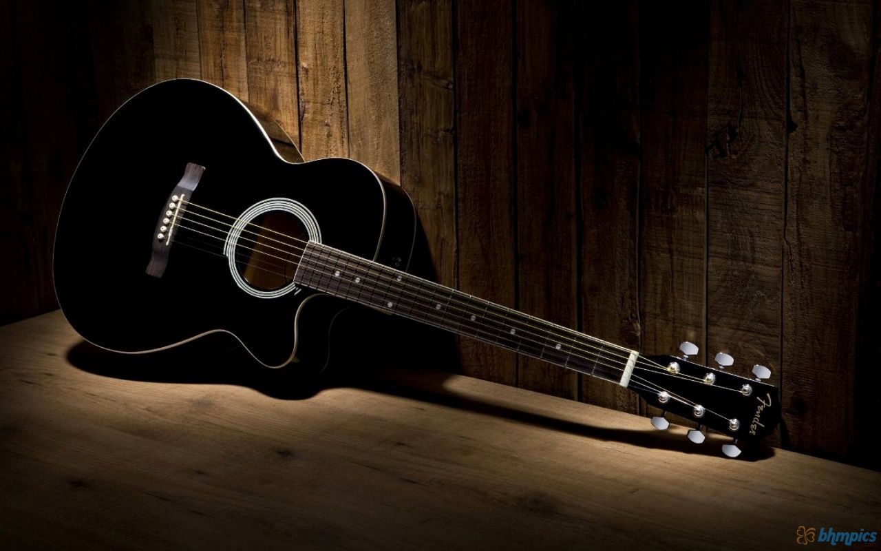 A black guitar sitting on top of wooden wall - Guitar