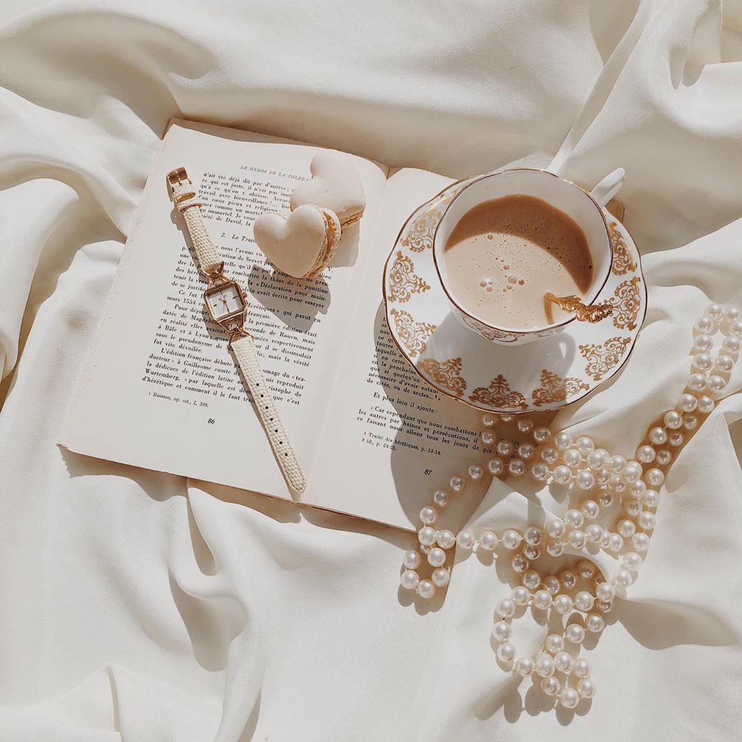 A book, coffee and pearls on top of white bedding - Champagne
