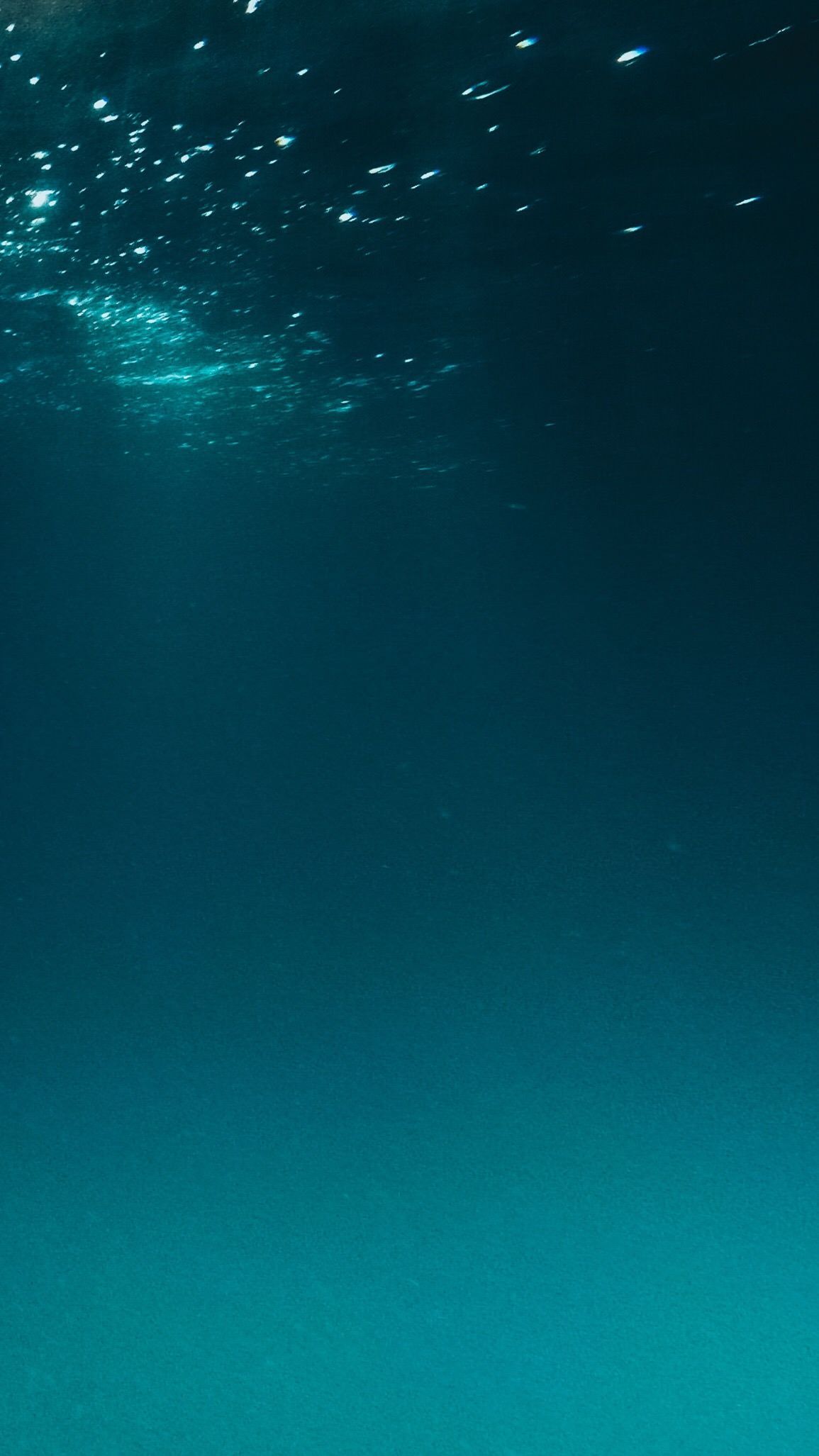 A dark blue and turquoise underwater scene with light shining through the water. - Underwater