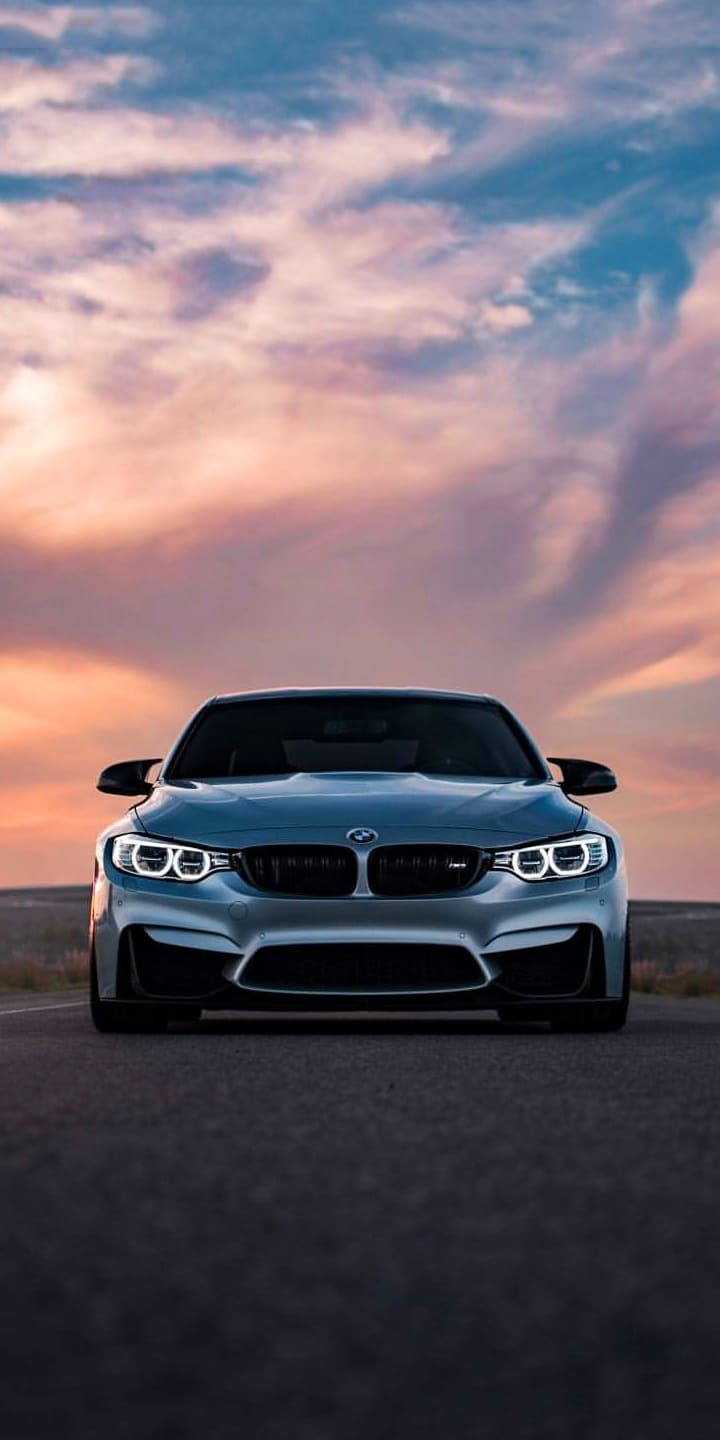 IPhone wallpaper of a silver BMW M4 on a road with a sunset in the background - BMW