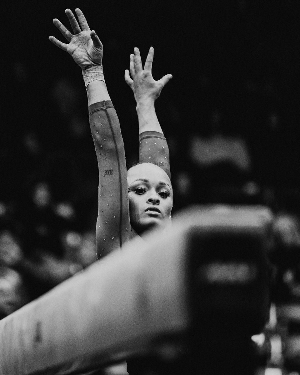 A gymnast raises her hands above her head during a routine. - Gymnastics