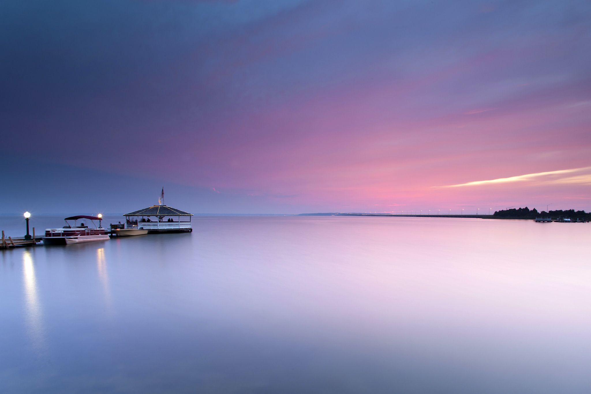 A docked boat sits on the water under a pink and blue sky. - Calming