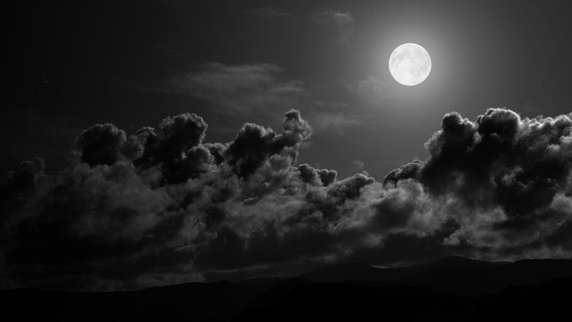 A full moon shines through the clouds in a black and white photo. - Gray