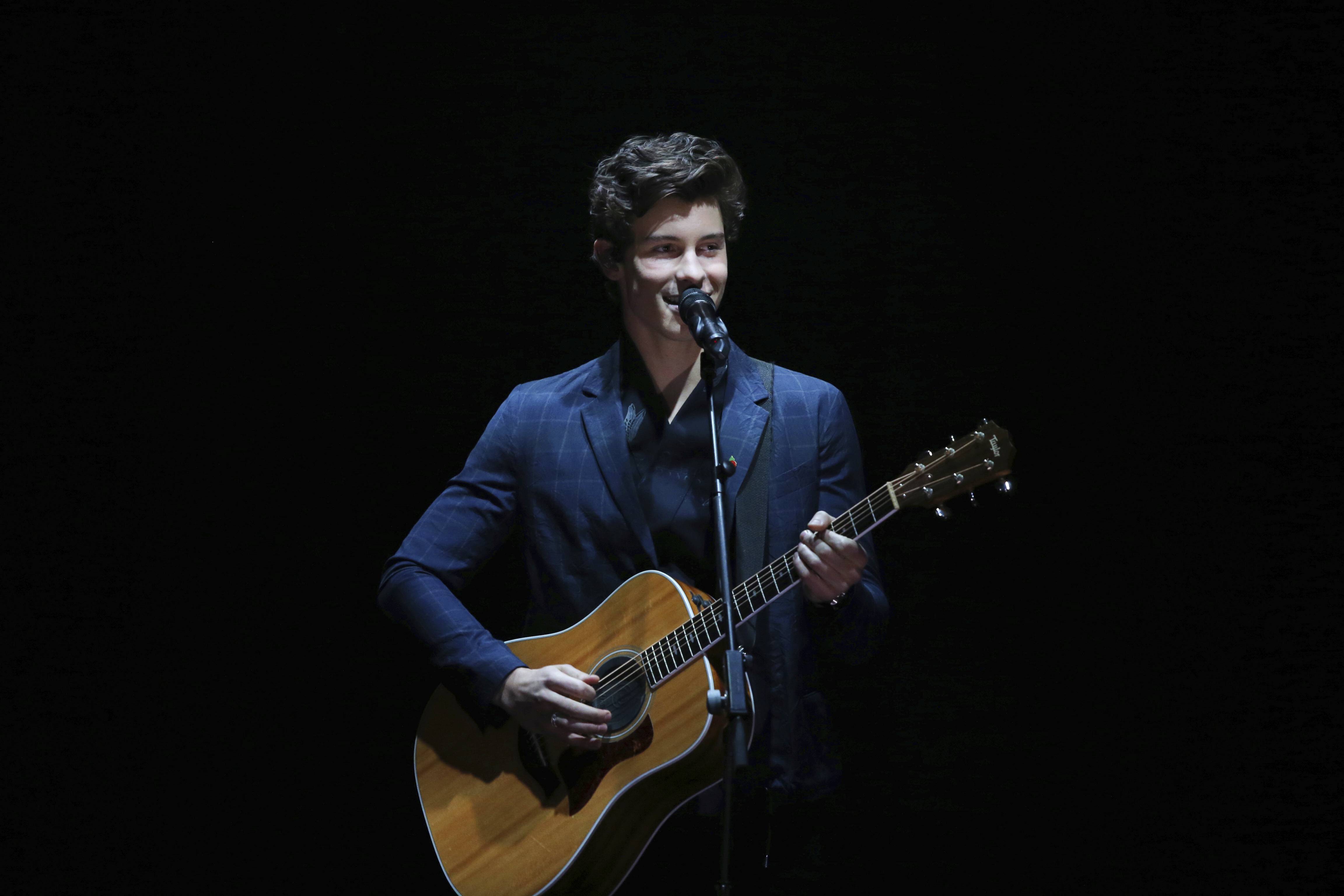 A man playing an acoustic guitar in front of microphone - Shawn Mendes