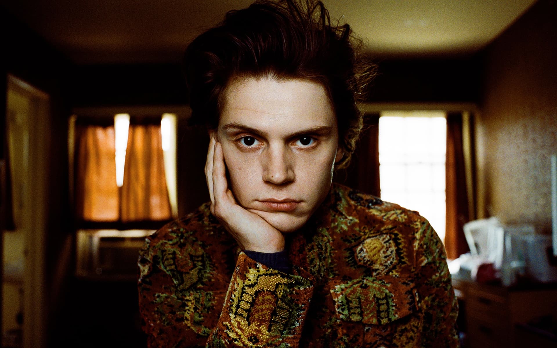 A young man with his head resting on his hand, staring into the camera - Evan Peters