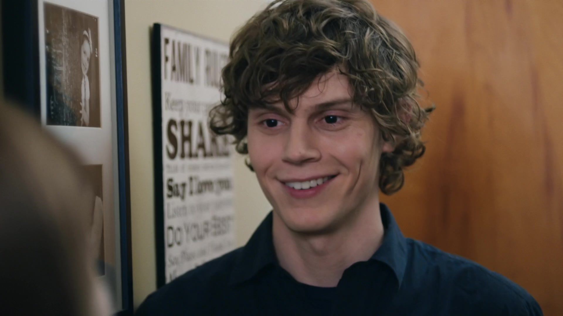 A young man with curly hair smiles at the camera - Evan Peters